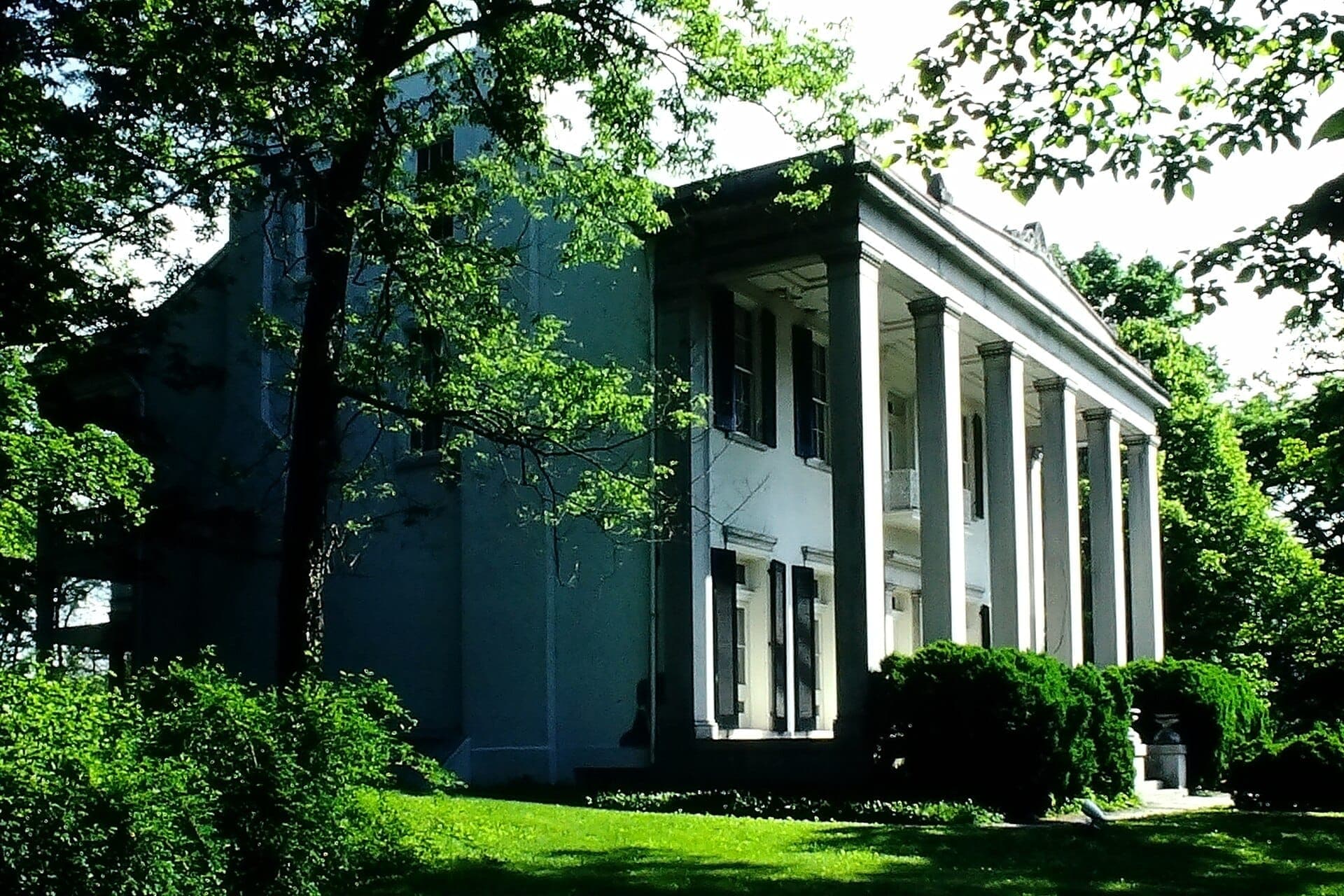 The Belle Meade mansion, a grand white Greek Revival building with tall columns, surrounded by lush green trees and manicured lawns.
