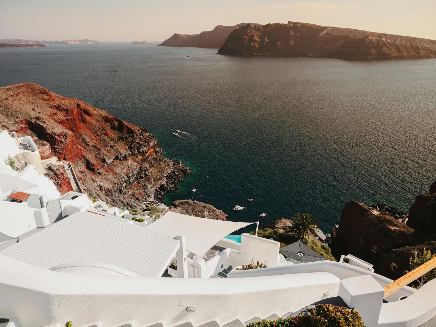 Widok na dramatyczne wybrzeże Santorini z uderzającymi czerwonymi klifami wulkanicznymi, białymi budynkami i głęboko niebieskim morzem, przywołującym Red Beach i White Beach.