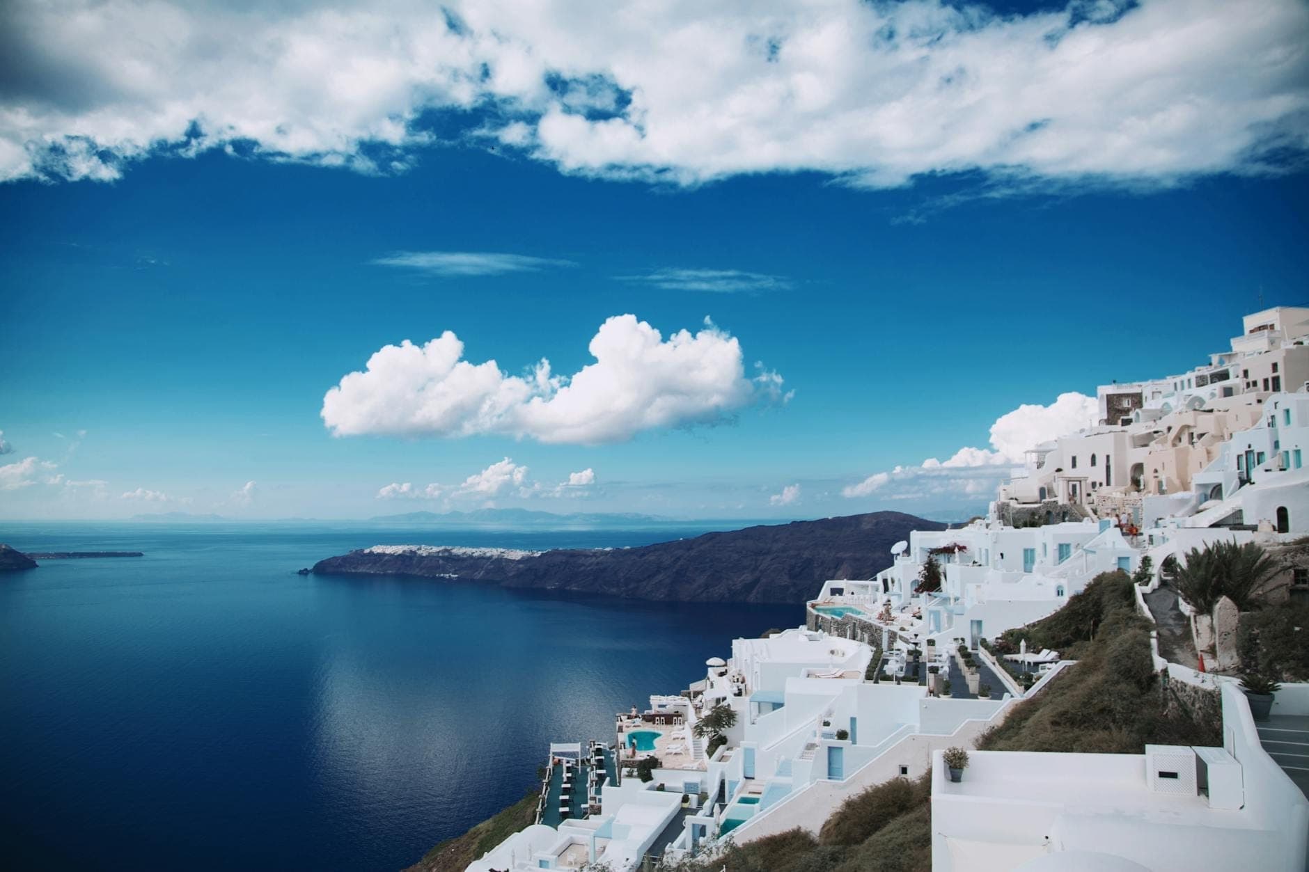 Zapierający dech w piersiach widok z klifu na białe budynki z widokiem na głęboko niebieskie morze i kalderę Santorini w pogodny, słoneczny dzień.
