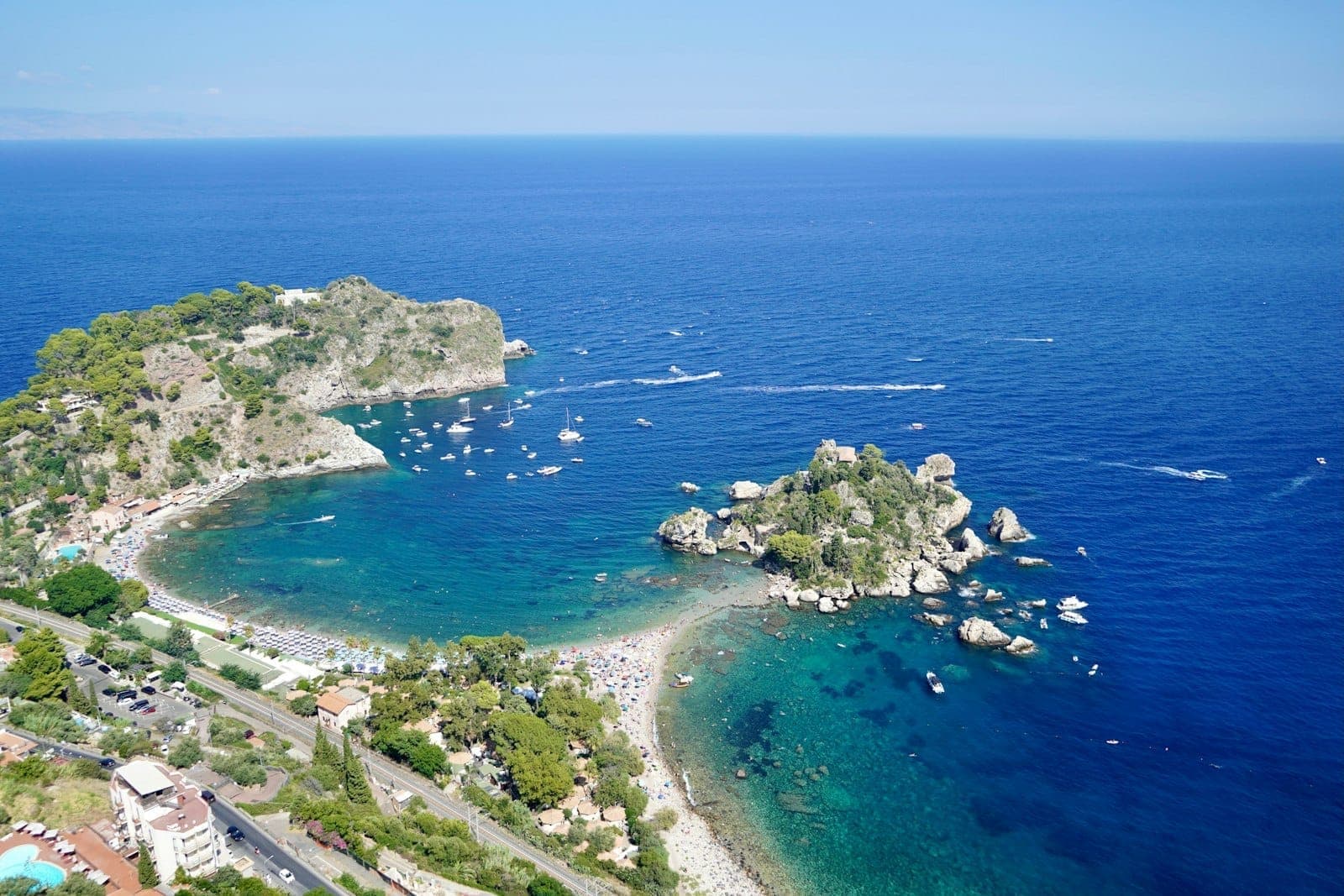 Aerial na view ng Isola Bella at turquoise na tubig malapit sa Taormina, na may mga dalampasigan, bangka, at berdeng burol sa kahabaan ng Ionian coast ng Sicily.