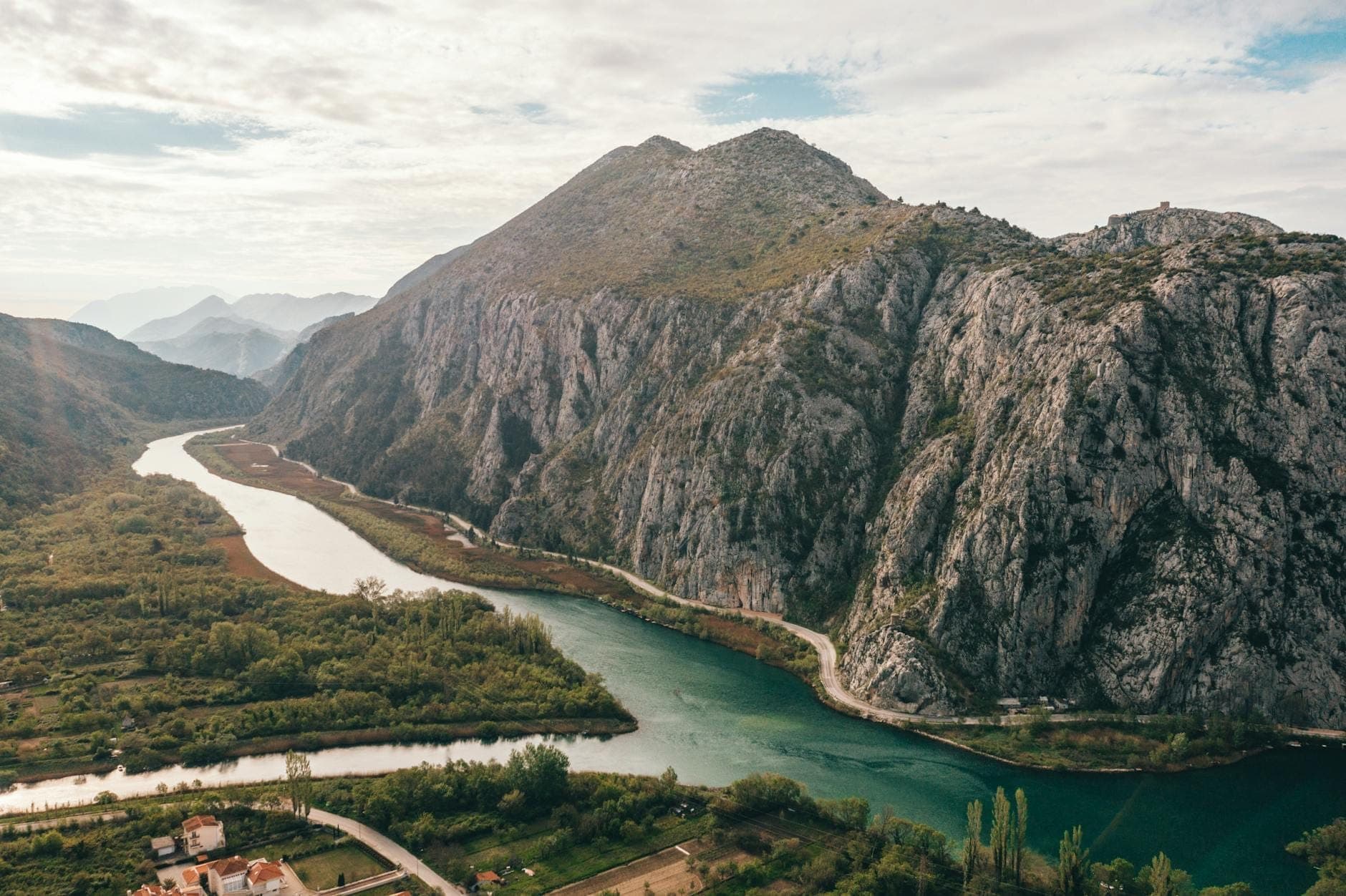 Une large rivière serpente à travers un canyon vert spectaculaire, avec des falaises rocheuses escarpées et un paysage montagneux sous un ciel partiellement nuageux.