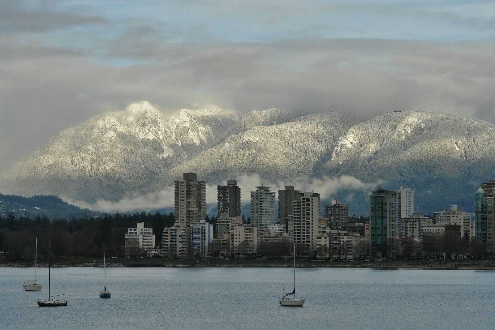 เส้นขอบฟ้าของ Vancouver พร้อมริมน้ำ เรือใบ และภูเขาที่ปกคลุมด้วยหิมะในพื้นหลังในวันที่มีเมฆมาก