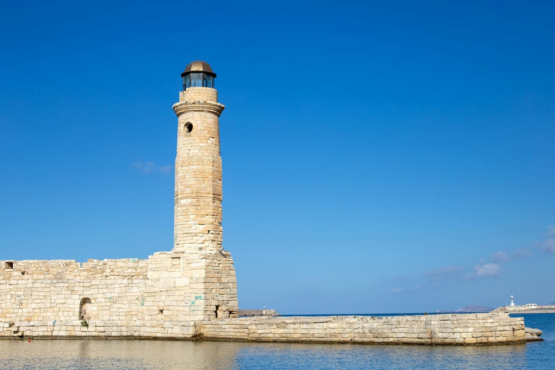 Steinerner Leuchtturm im venezianischen Hafen von Rethymno unter klarem blauem Himmel, ein berühmtes Wahrzeichen ideal für Tagesausflüge von Rethymno, Kreta.