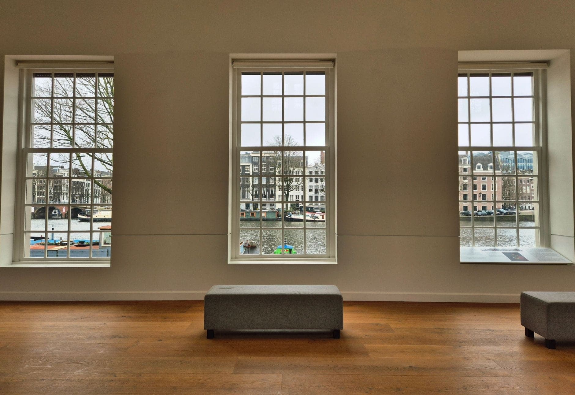 Innenansicht eines ruhigen Museumsraums in Amsterdam mit großen Fenstern mit Blick auf den Kanal und historische Gebäude.