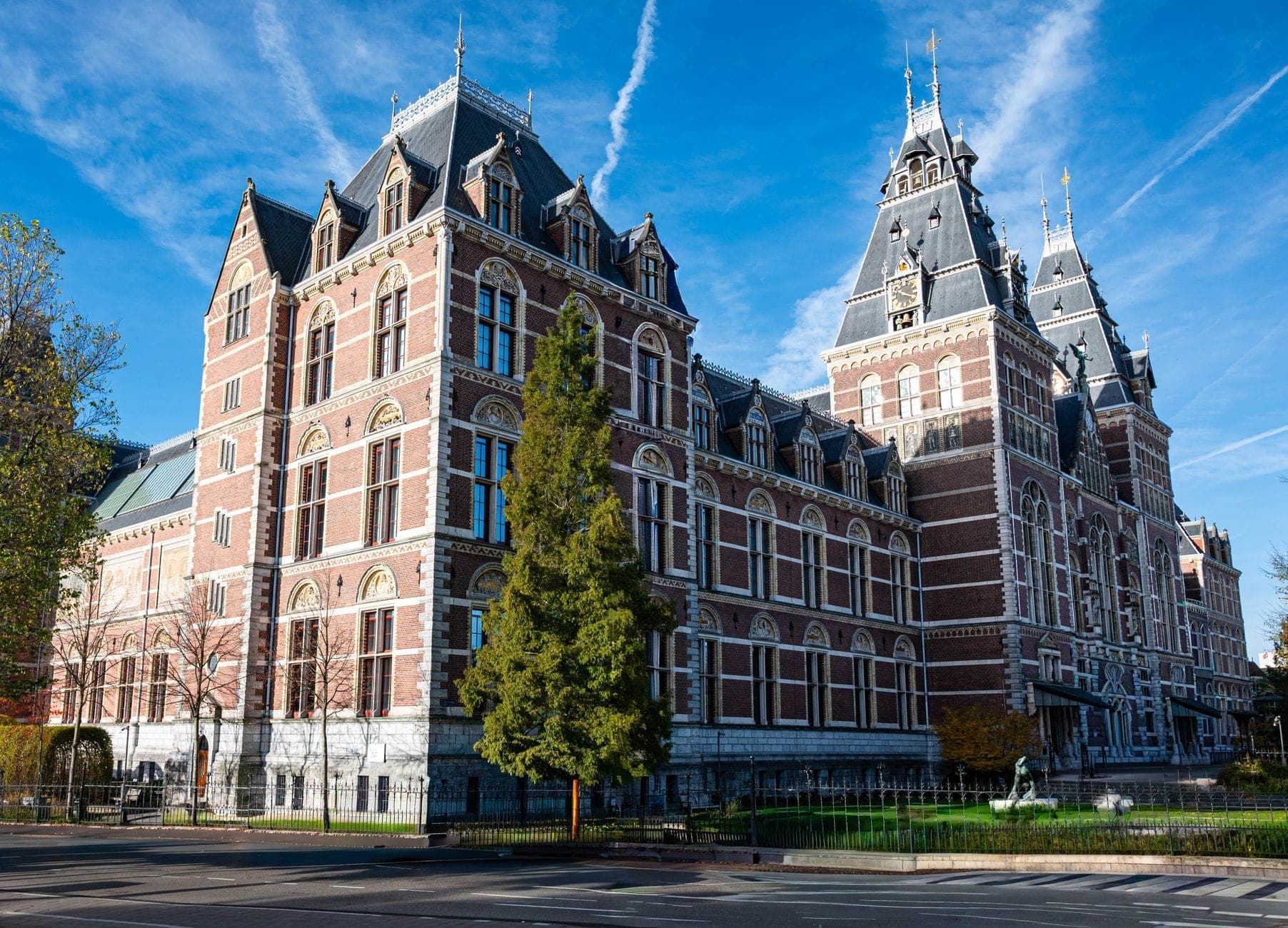 Großes, verziertes Backsteinmuseumsgebäude mit Türmchen und Türmen unter blauem Himmel, wahrscheinlich das Rijksmuseum in Amsterdam.