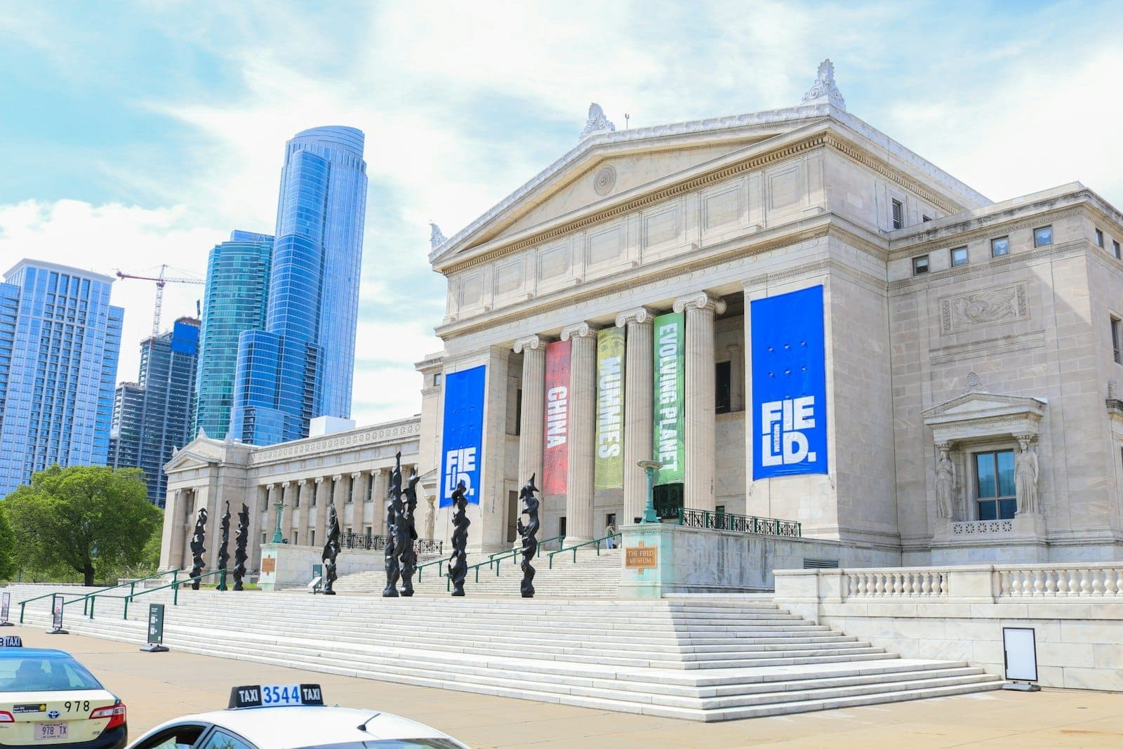 The Field Museum’s impressive neoclassical facade with columns and banners, set against Chicago’s skyline on a sunny day, inviting visitors to explore.