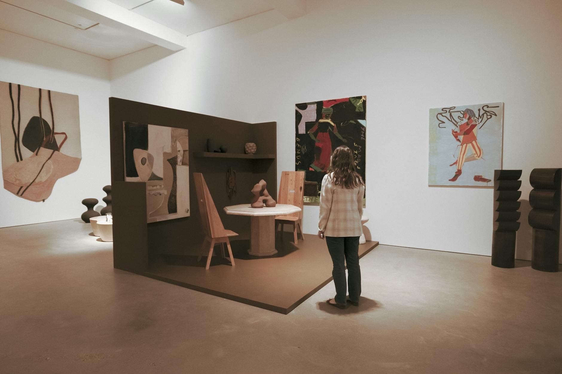 Person betrachtet zeitgenössische Kunstinstallationen und moderne Gemälde in einem sauberen, gut beleuchteten Galerieraum.