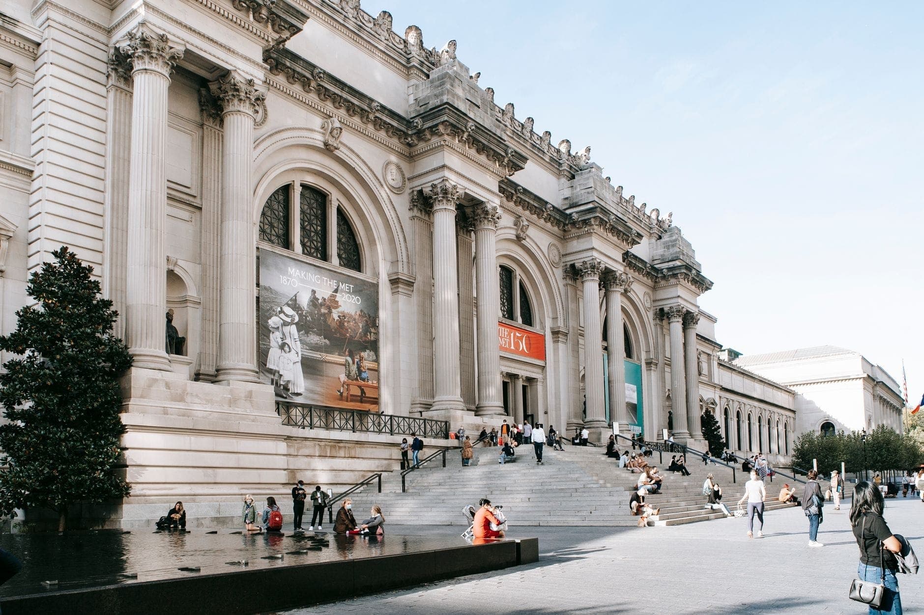 มุมมองกว้างของทางเข้า Metropolitan Museum of Art บน Fifth Avenue พร้อมผู้คนที่นั่งและเดินบนบันไดอันเป็นสัญลักษณ์