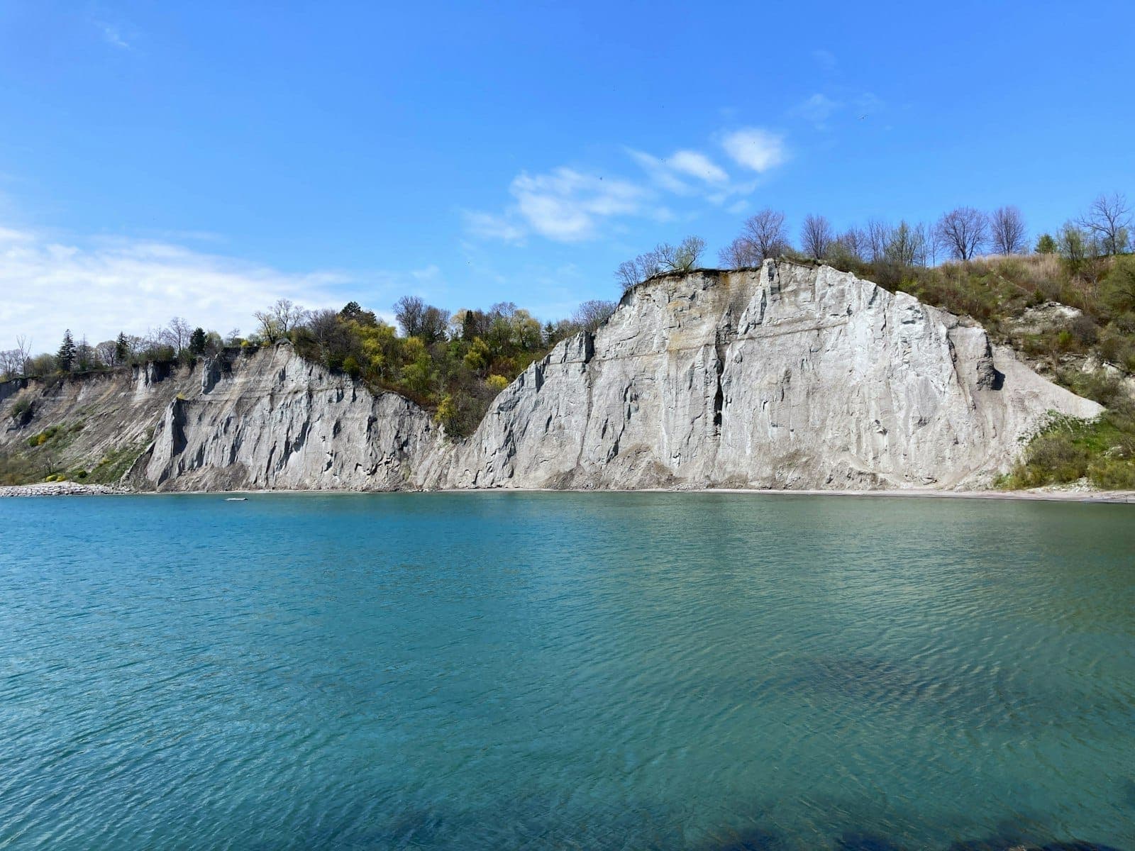 Steep white cliffs rise dramatically above blue water under a clear sky, with sparse trees atop the bluffs in Toronto.