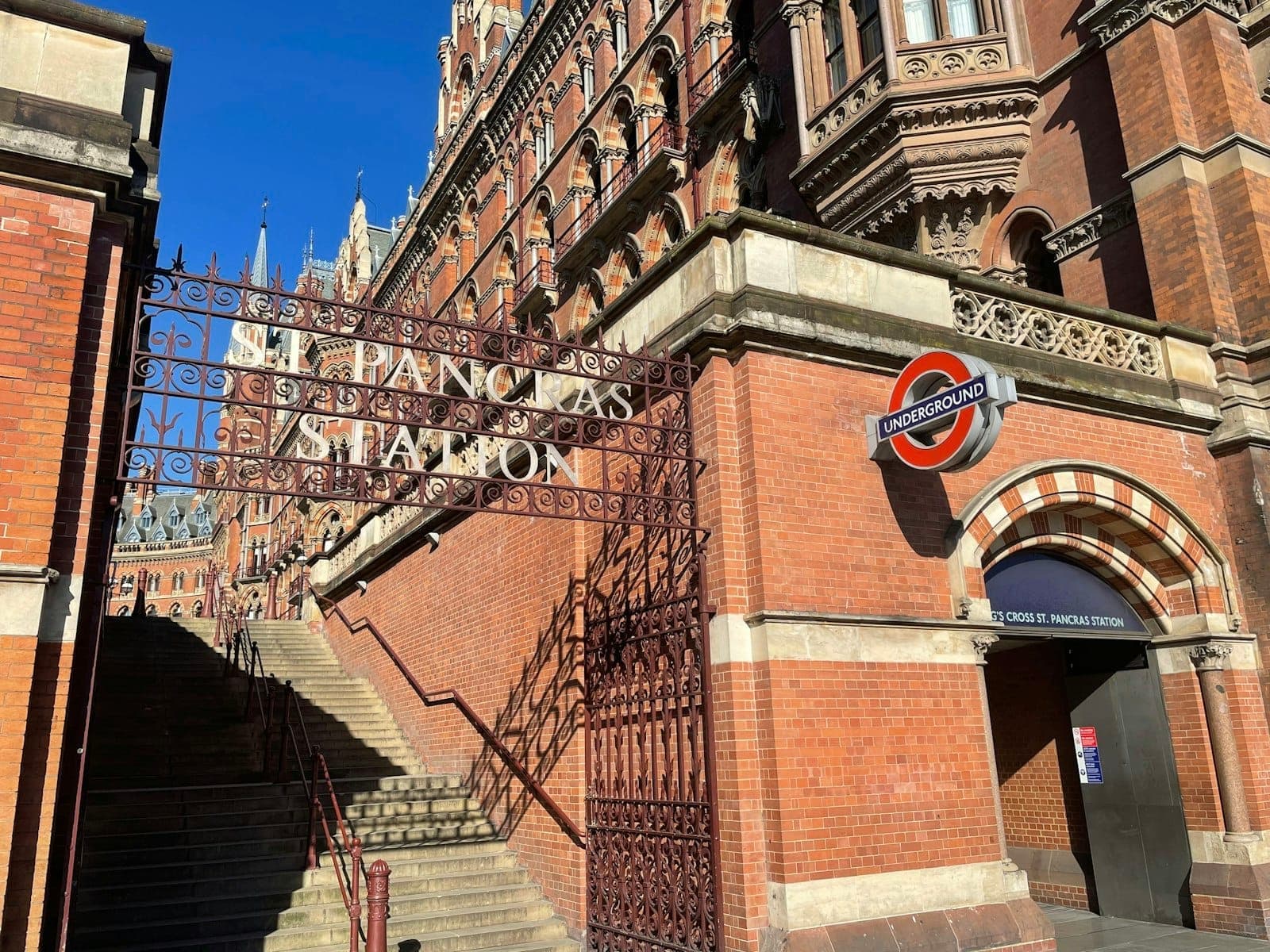 Vista dell'ingresso della St Pancras Station a Londra con architettura in mattoni rossi e insegna dell'Underground sotto un cielo azzurro limpido