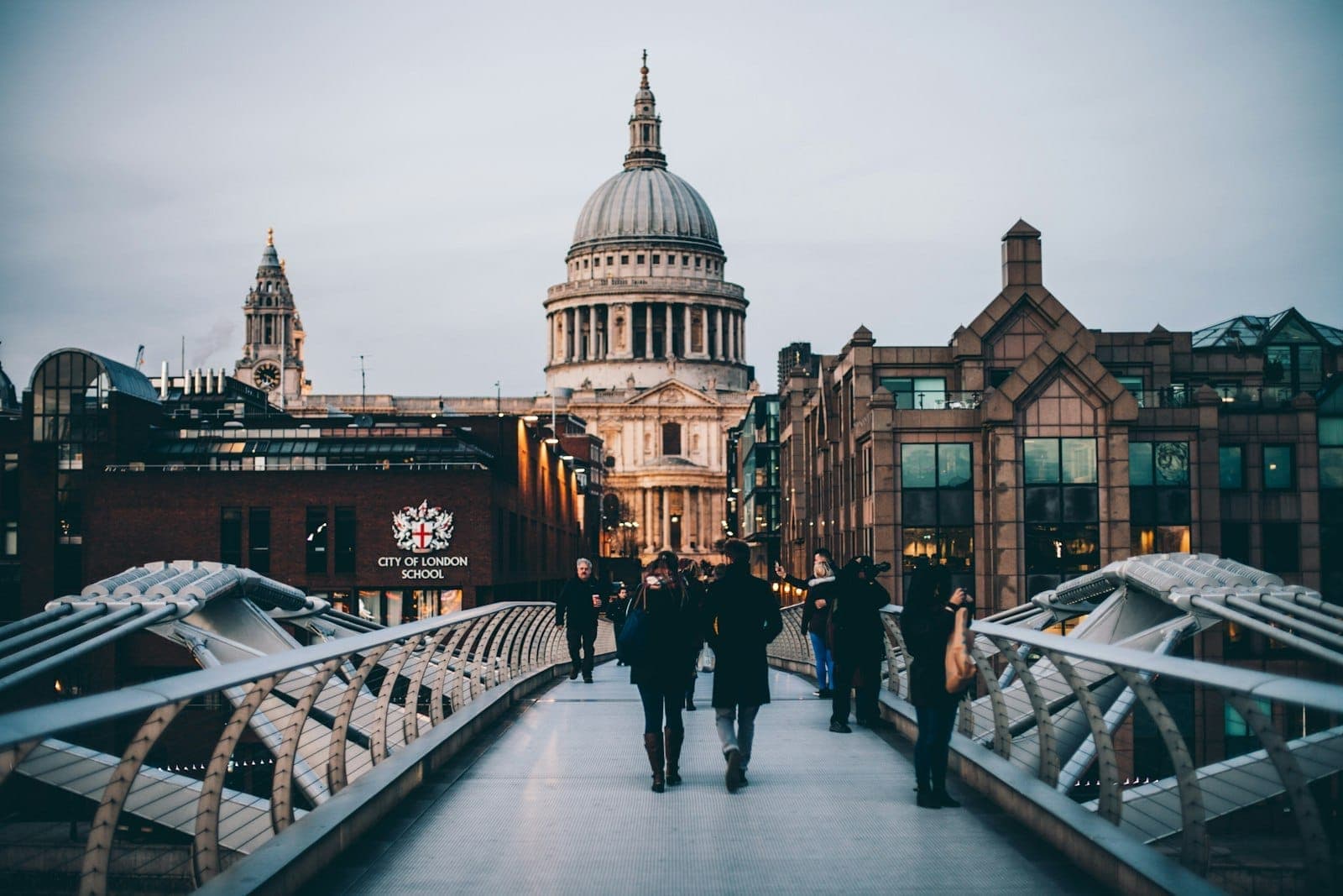 Vista della Cattedrale di St Paul's dal Millennium Bridge al crepuscolo, con persone che camminano ed edifici della città su entrambi i lati.
