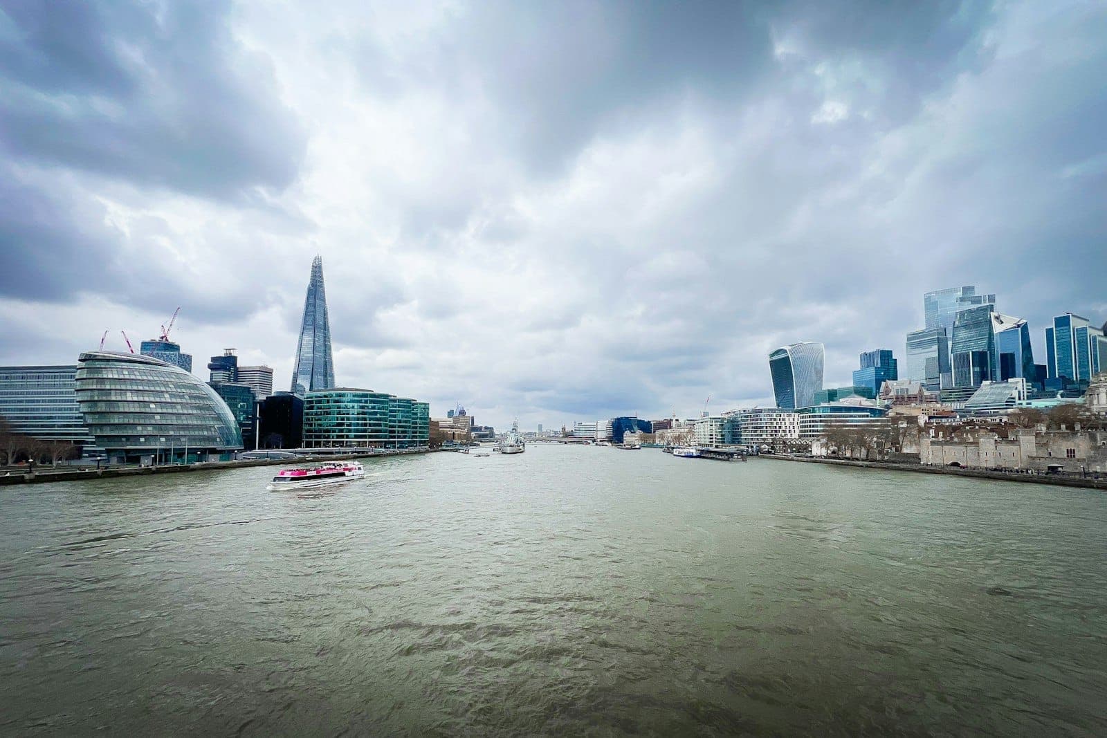 Vista ampia del fiume Tamigi a Londra con il moderno skyline della città, cielo nuvoloso e il grattacielo Shard visibile.