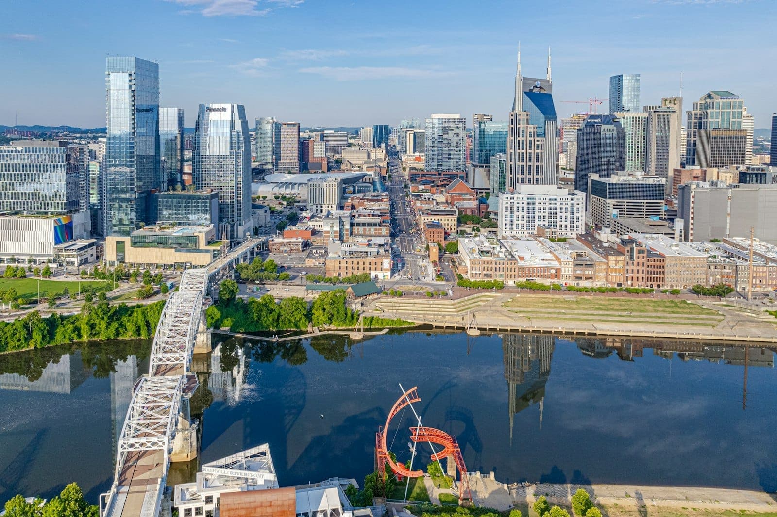 Widok z lotu ptaka na panoramę śródmieścia Nashville, rzekę Cumberland, zielone drzewa i słoneczne błękitne niebo ukazujące piękną pogodę i miejsca charakterystyczne miasta.