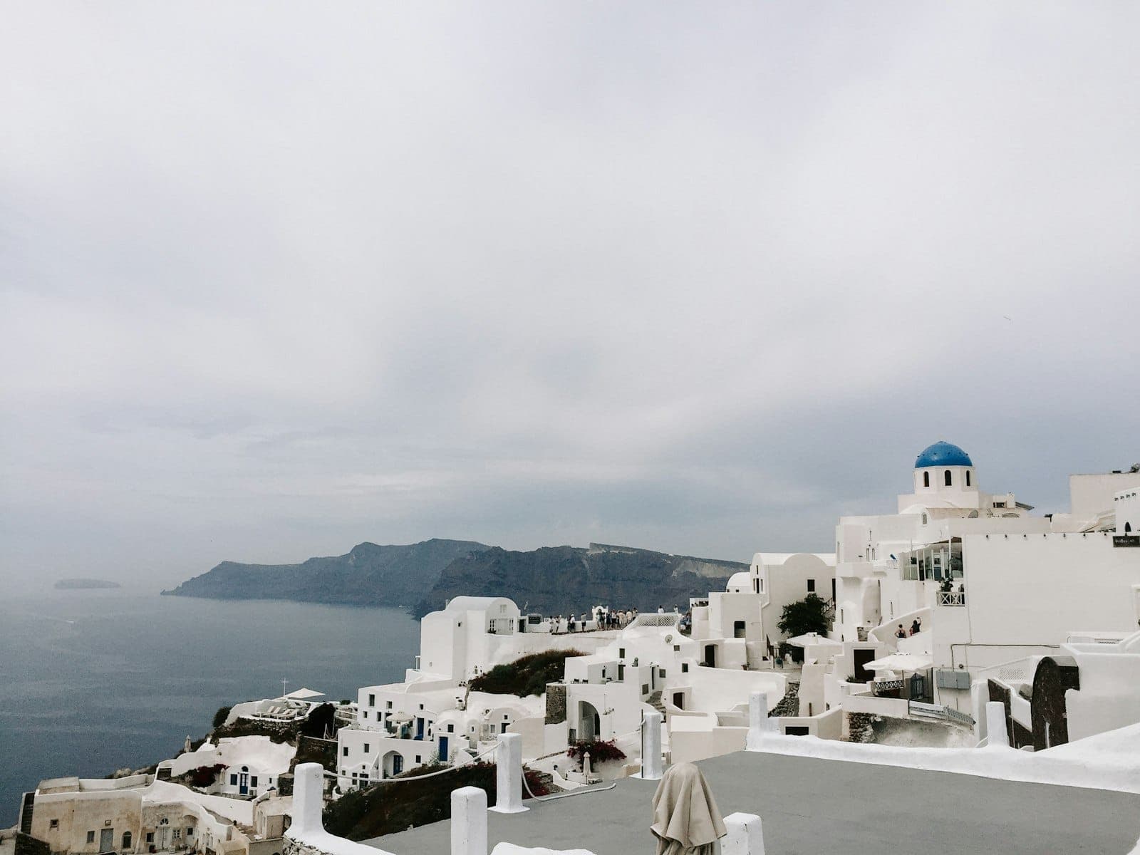 Icônicos edifícios caiados de branco com cúpulas azuis com vista para o mar e os penhascos em Santorini sob um céu nublado.