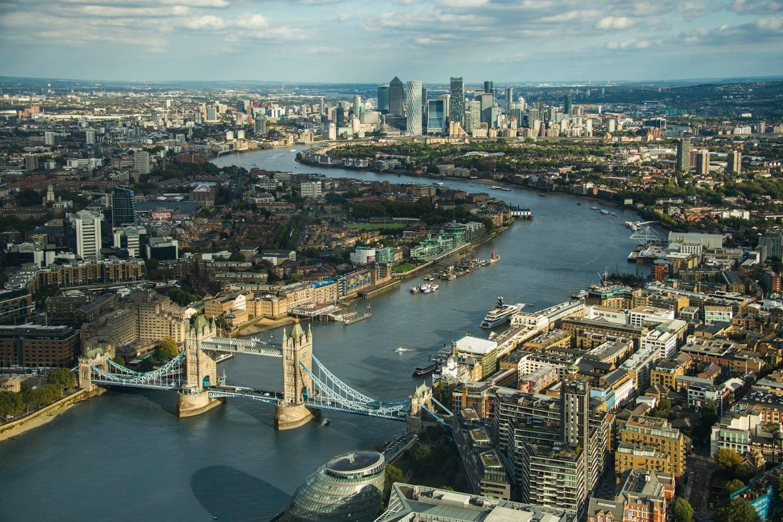 Vista aerea del Tower Bridge sul fiume Tamigi, con lo skyline di Londra e le rive del fiume ben visibili.