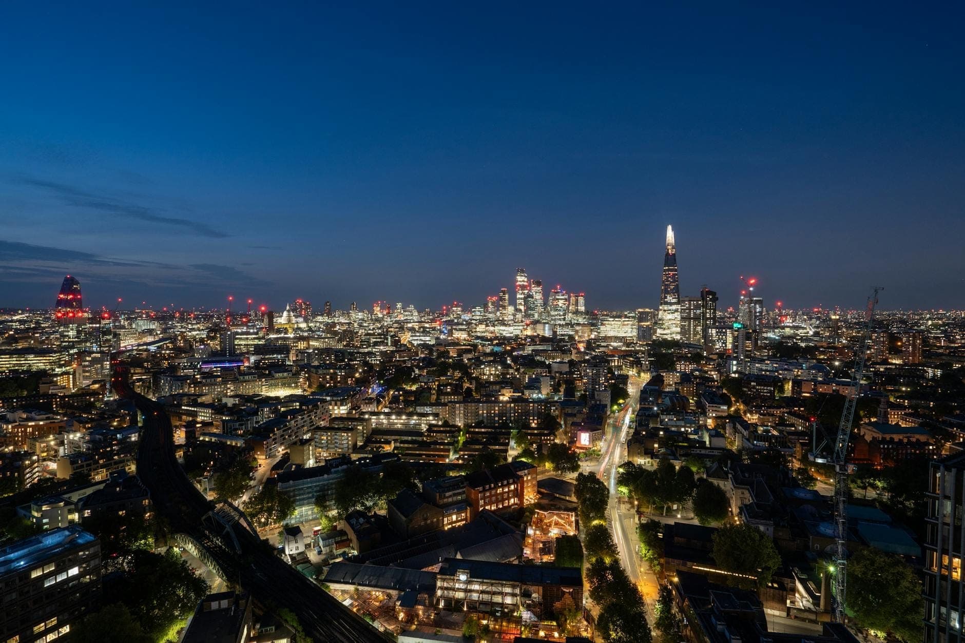 Skyline di Londra al crepuscolo con grattacieli illuminati, The Shard e gli edifici della città sotto un cielo blu intenso, con le luci della metropoli in primo piano.