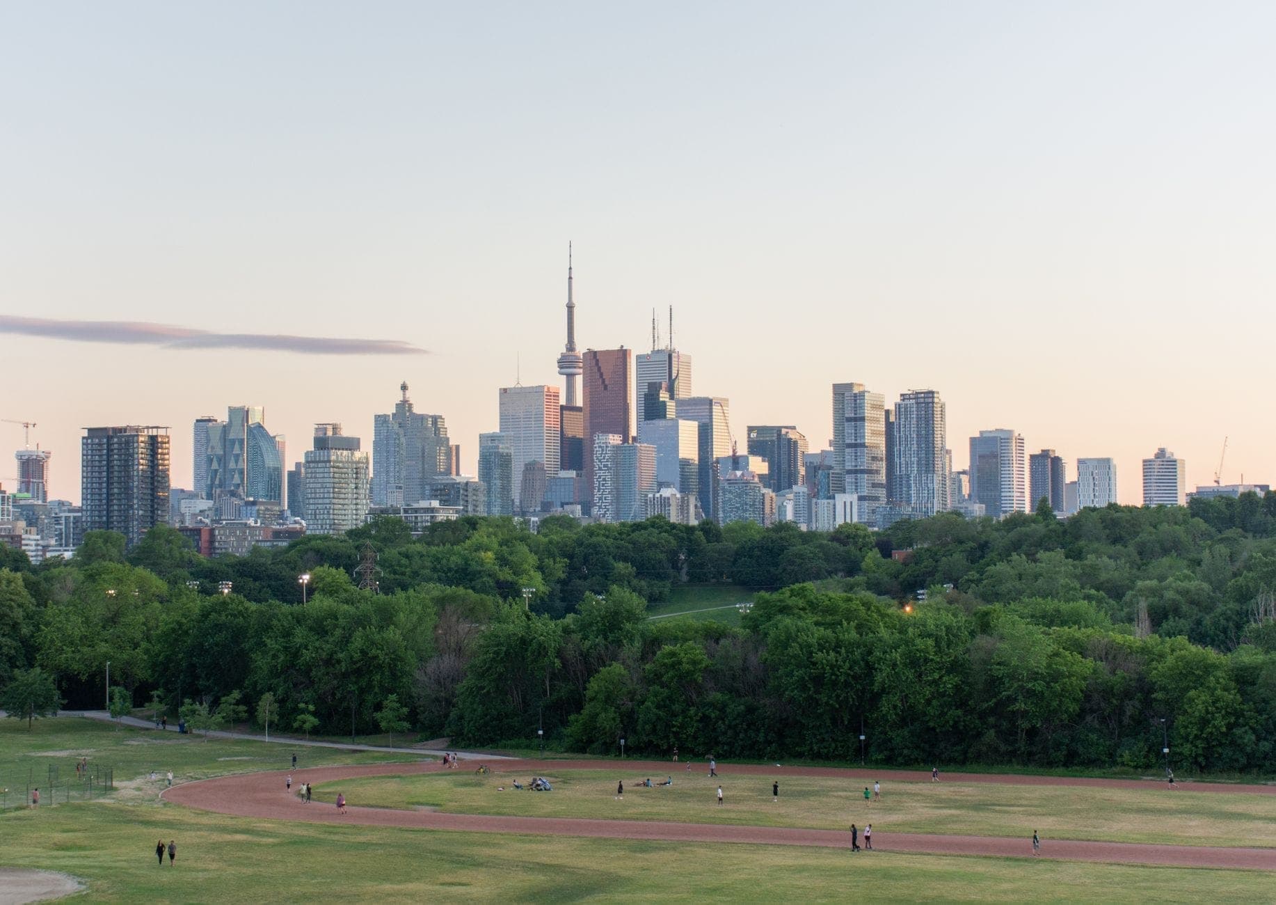 Vista panorámica desde un parque en lo alto de una colina con césped que mira sobre los árboles hacia el horizonte de Toronto, con la CN Tower y los edificios de la ciudad visibles al atardecer.