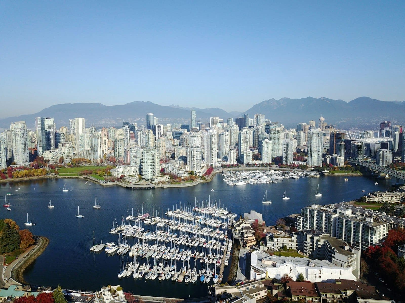 มุมมองทางอากาศของท่าจอดเรือ Vancouver พร้อมเรือยอทช์ เส้นขอบฟ้าของเมืองสมัยใหม่ ภูเขาในพื้นหลัง และน้ำในเบื้องหน้าในวันที่อากาศแจ่มใส