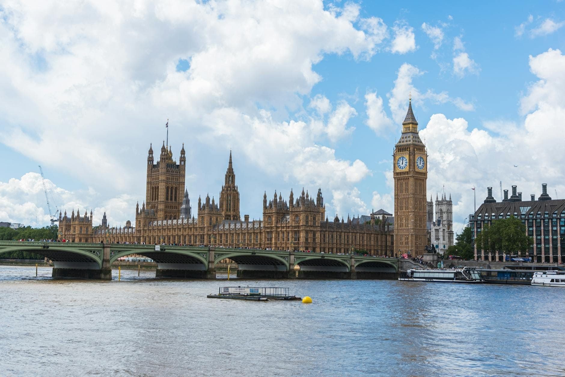 Big Ben und der Palast von Westminster in London mit der Westminster Bridge über der Themse an einem hellen, leicht bewölkten Tag.