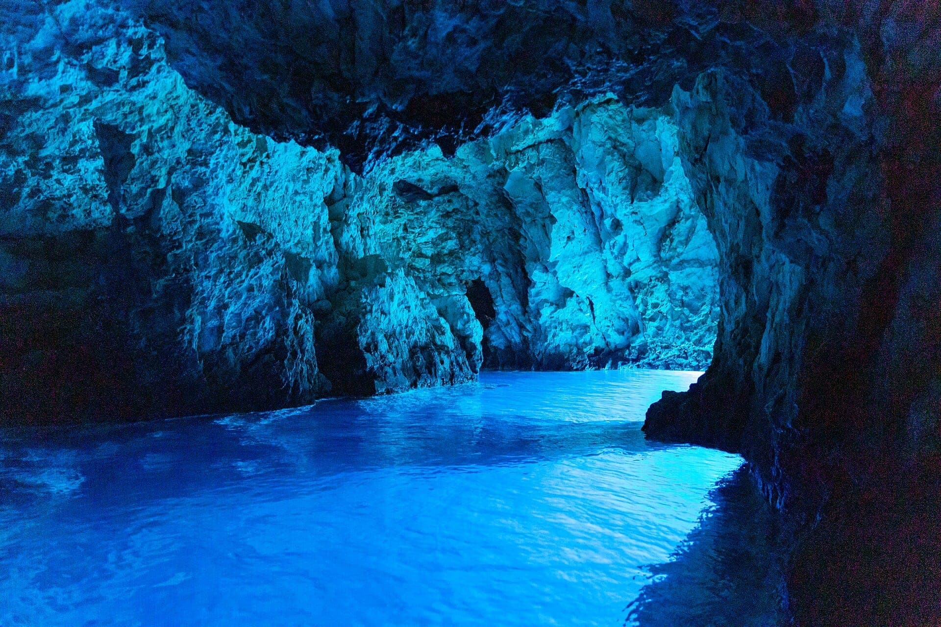 La lumière du soleil se reflète sur l'eau turquoise à l'intérieur de la rocheuse Blue Cave de Biševo, illuminant les parois de pierre d'une vive lueur bleue.