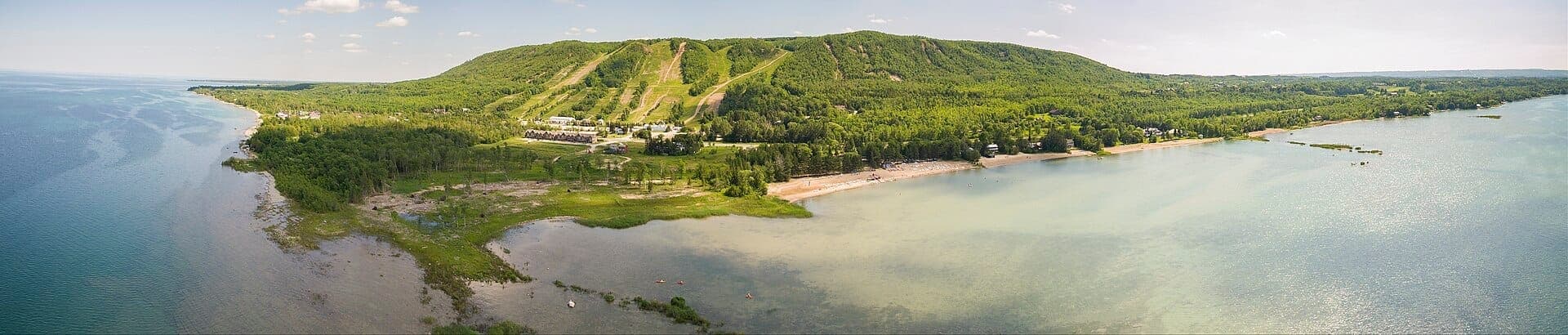 Vista aérea de Blue Mountain y Collingwood con pistas de esquí, exuberante bosque verde, costa y la brillante Georgian Bay en un día soleado.