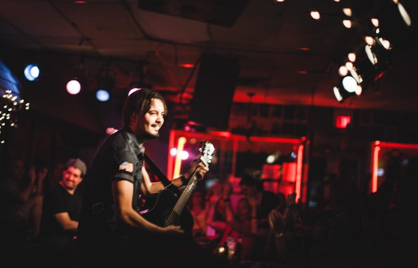 Musician performing with an acoustic guitar at the Bluebird Cafe in Nashville, surrounded by warm stage lighting and an intimate audience.