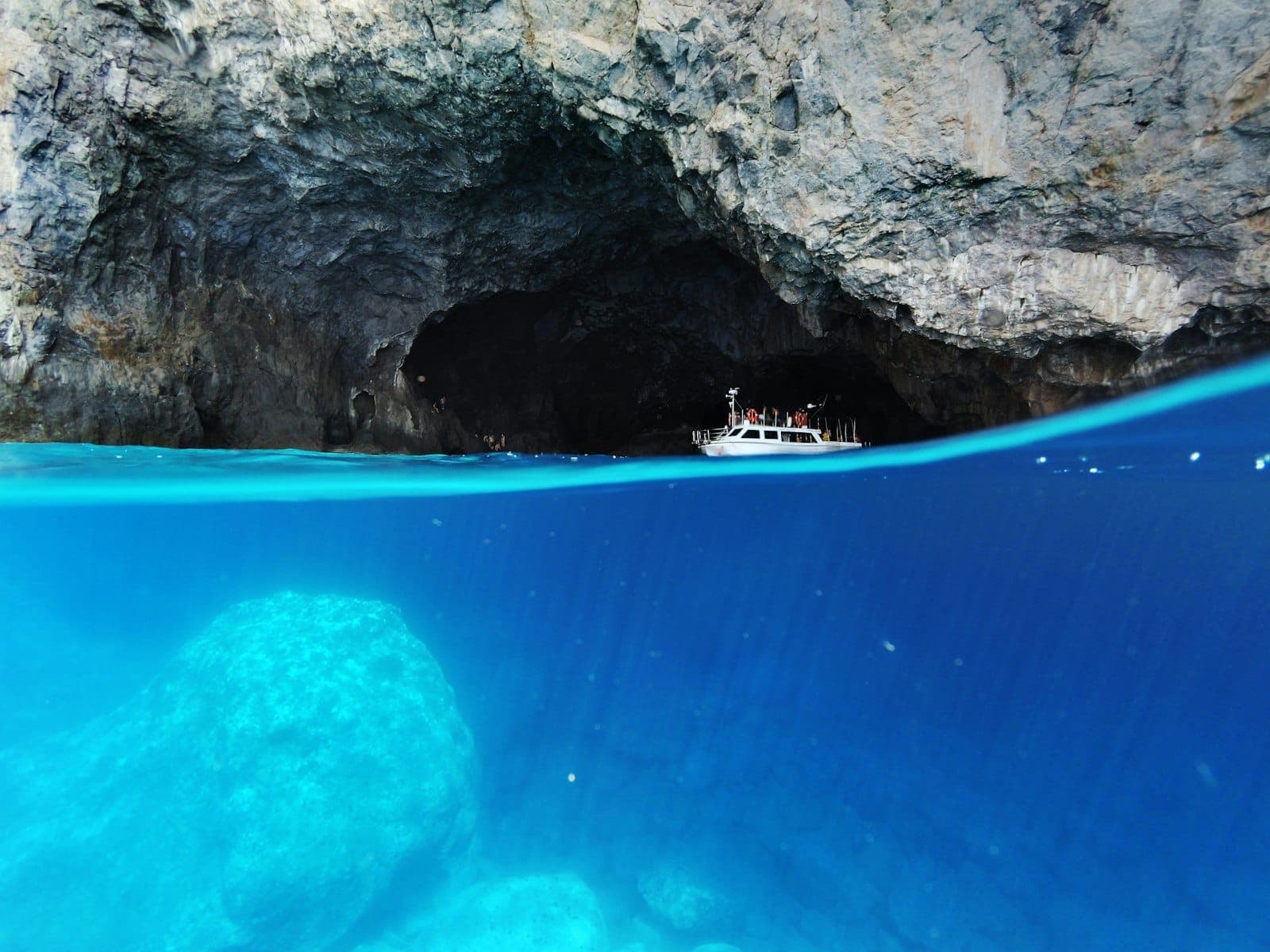 Una barca galleggia all'ingresso della Grotta Azzurra con l'acqua turchese brillante sotto e le pareti rocciose della grotta sopra, catturando l'emozione dei tour alle isole da Spalato.
