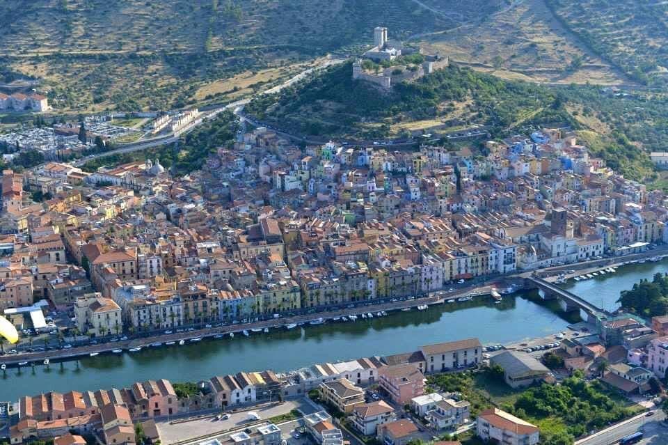 Vista aérea de Bosa, Cerdeña, con coloridas casas a orillas del río, un castillo medieval en la colina y el río Temo atravesando la ciudad.