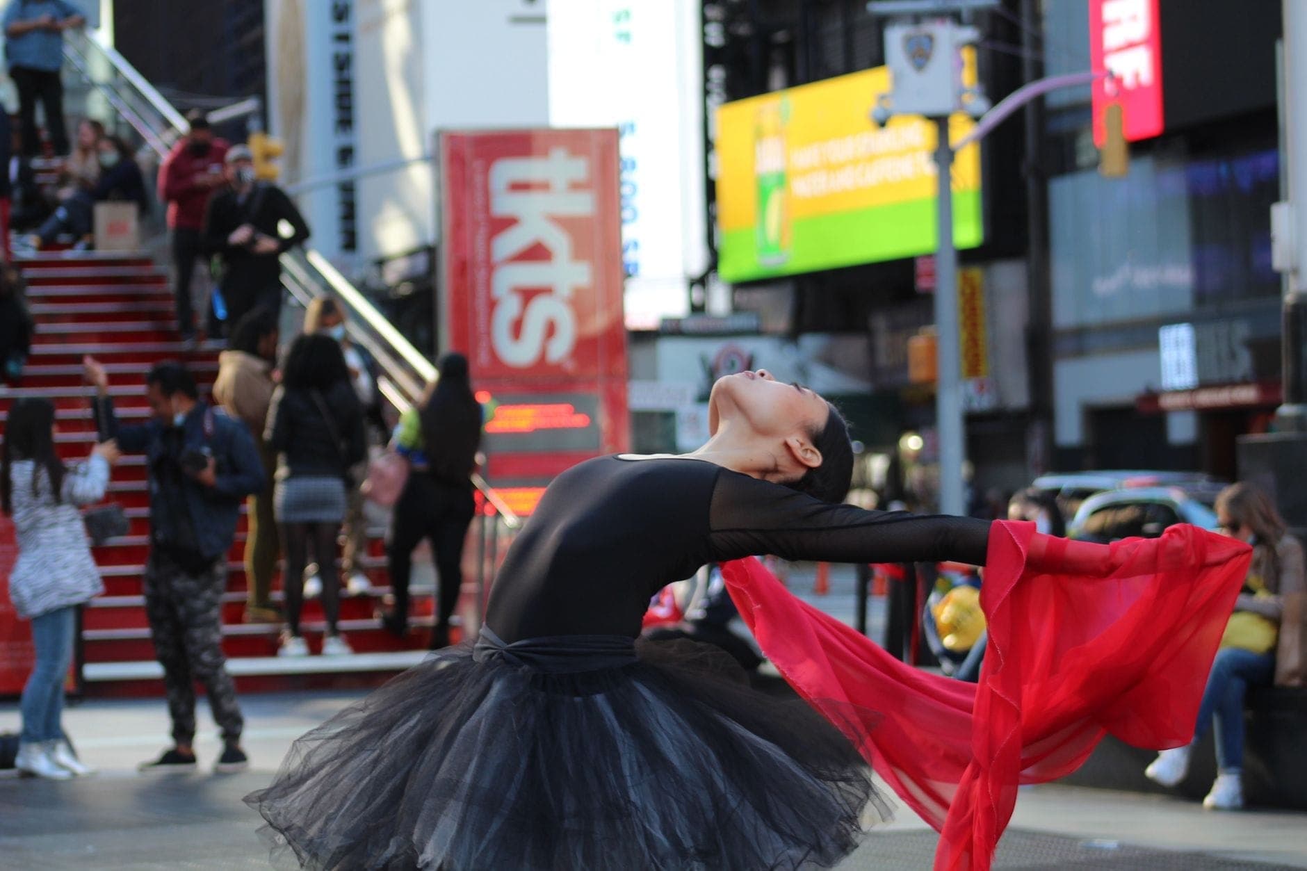 นักเต้นแสดงที่ Times Square โดยมีป้าย TKTS booth มองเห็นได้ในพื้นหลังและมีผู้คนอยู่ใกล้เคียง