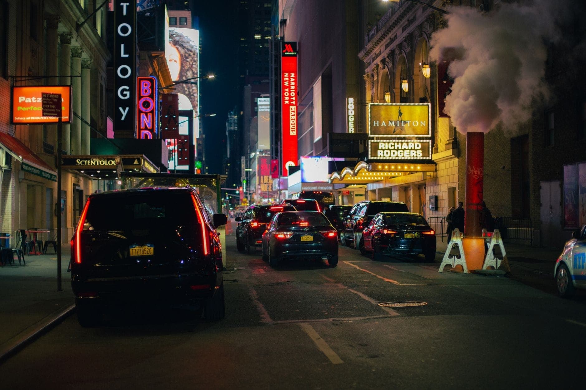 ทัศนียภาพถนนยามค่ำคืนใน Theater District ของนิวยอร์ก โดยมี Richard Rodgers Theatre และป้าย Hamilton ให้เห็นท่ามกลางรถยนต์และแสงไฟ