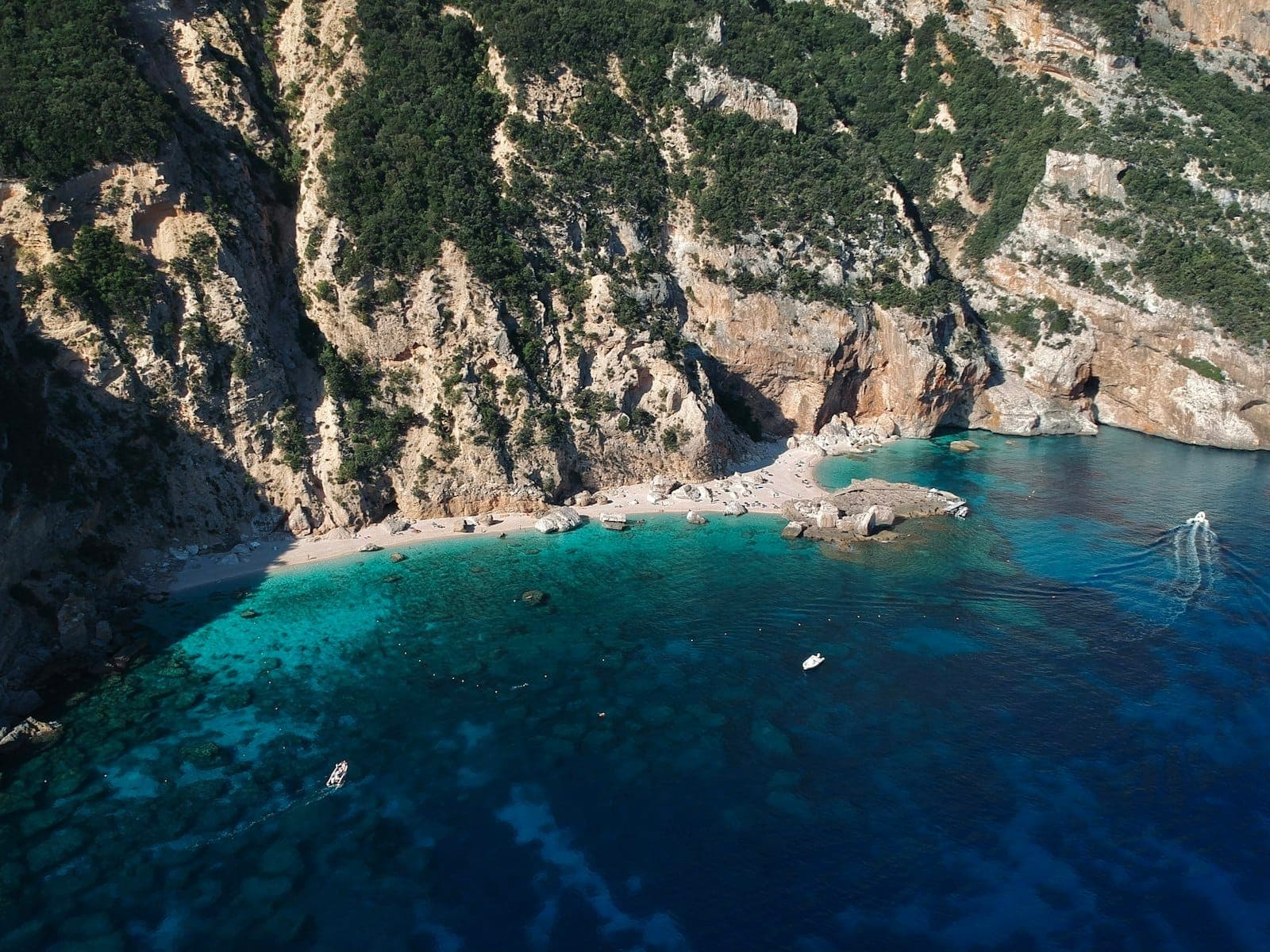 Luftaufnahme von Cala Mariolu mit zerklüfteten Kalksteinklippen, weißem Kieselstrand und lebhaft türkisfarbenem Wasser entlang des Golfs von Orosei.