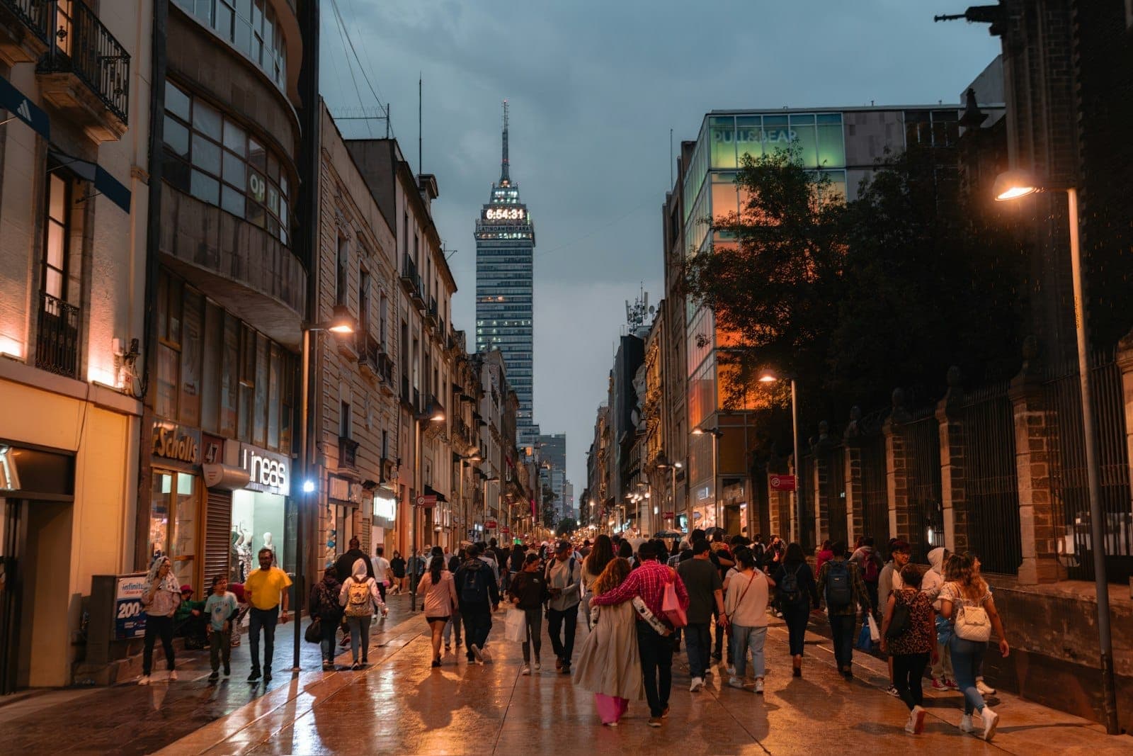 วิวค่ำของ Calle Madero ที่มีผู้คนแน่นขนัด สองข้างถนนปูด้วยตึกยุคอาณานิคม และฉากหลังเป็น Torre Latinoamericana ที่ส่องไฟสวย