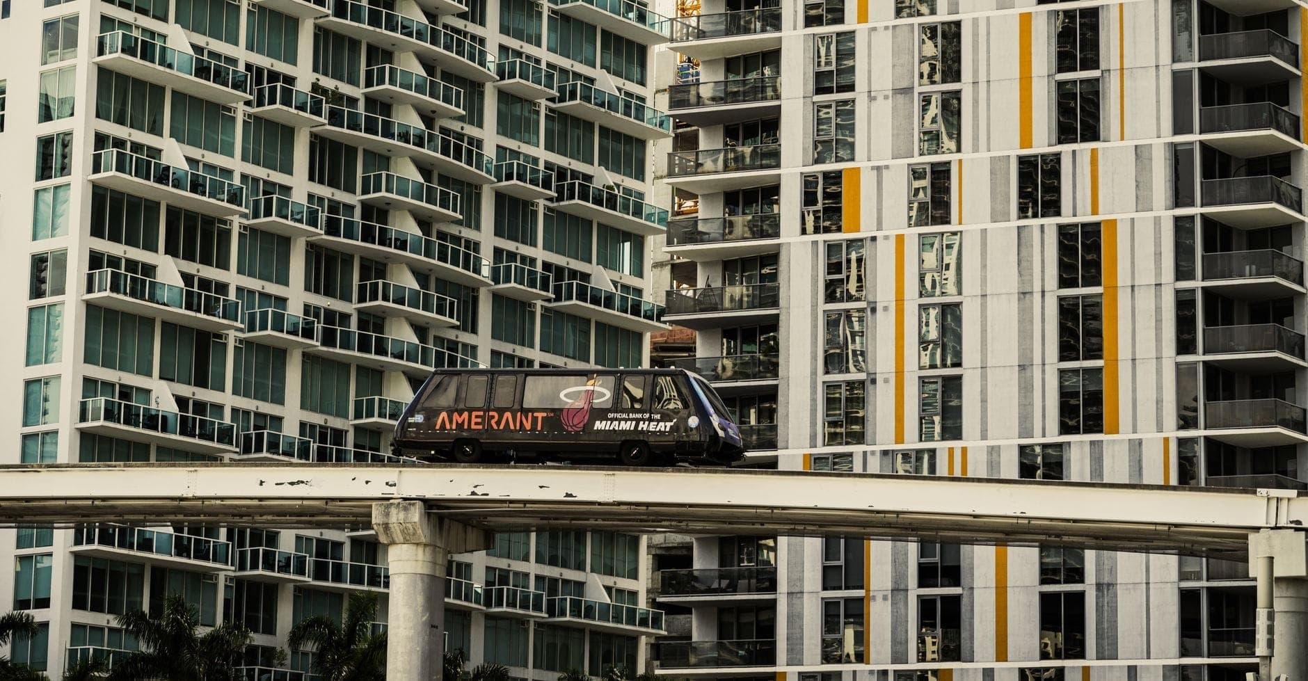 Miami Metromover train travels on elevated track past modern high-rise buildings in downtown Miami.