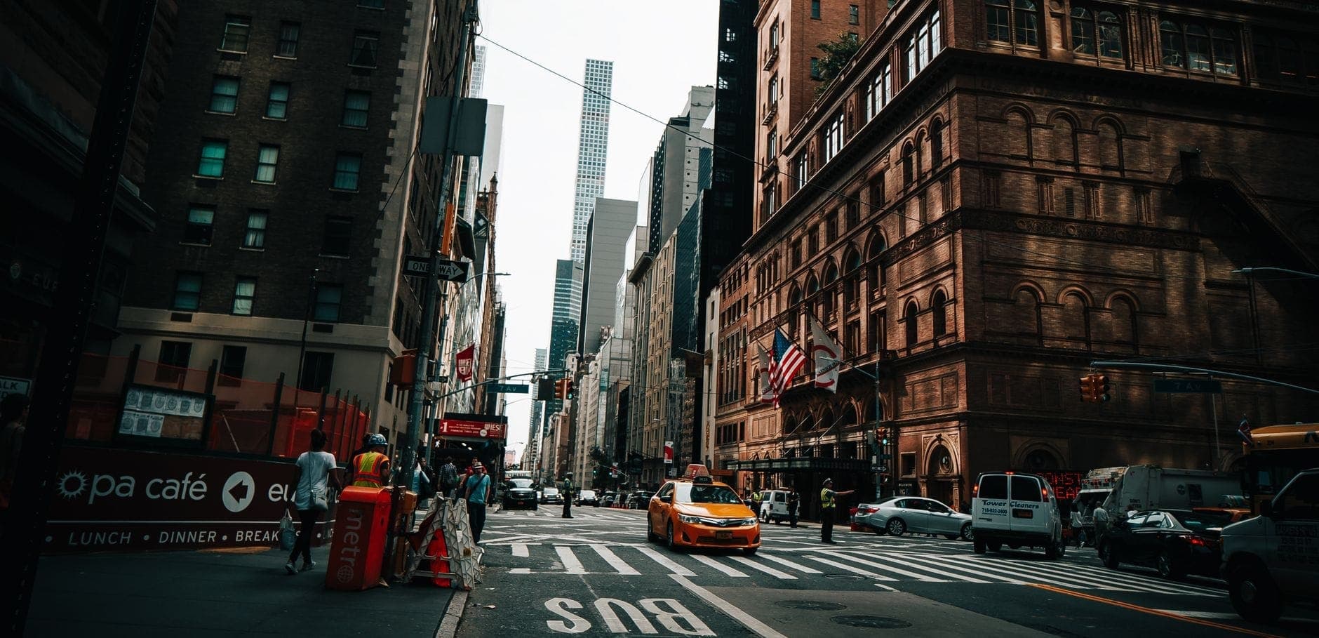 วิวถนนด้านหน้า Carnegie Hall อาคารอิฐโดดเด่นย่าน Midtown Manhattan วันครึกครื้น เหล่าแท็กซี่สีเหลือง คนเดินขวักไขว่ และตึกสูงฉากหลัง