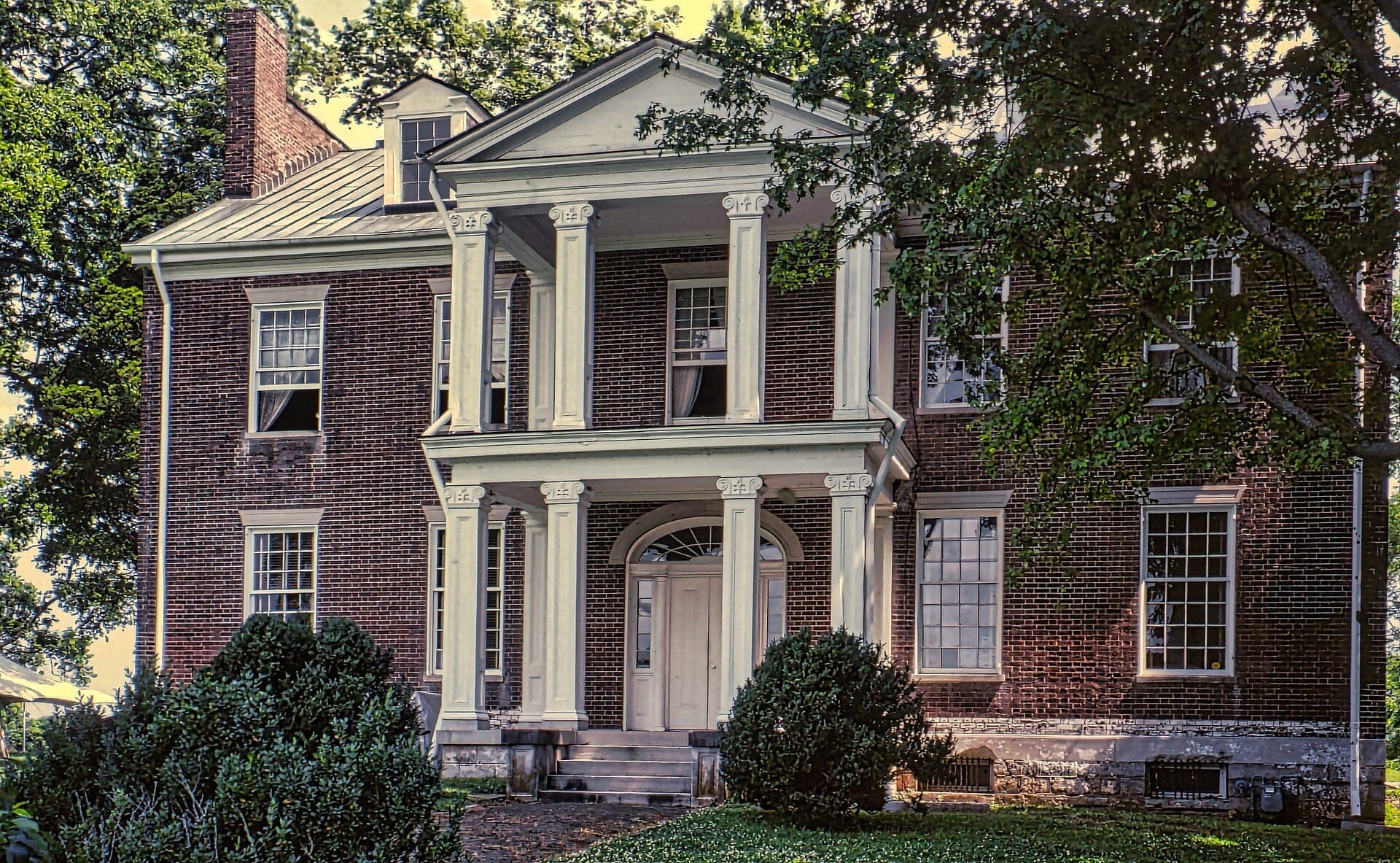 Vista frontal de la mansión Carnton en Franklin, Tennessee, con fachada de ladrillo rojo, columnas blancas y exuberante paisajismo verde.
