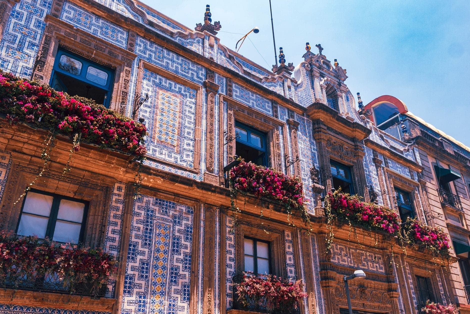 ด้านนอกของ Casa de los Azulejos ปกคลุมด้วยกระเบื้อง Talavera สีน้ำเงิน-ขาวอย่างประณีต มีดอกไม้บนระเบียงหน้าต่าง ท้องฟ้าสดใส