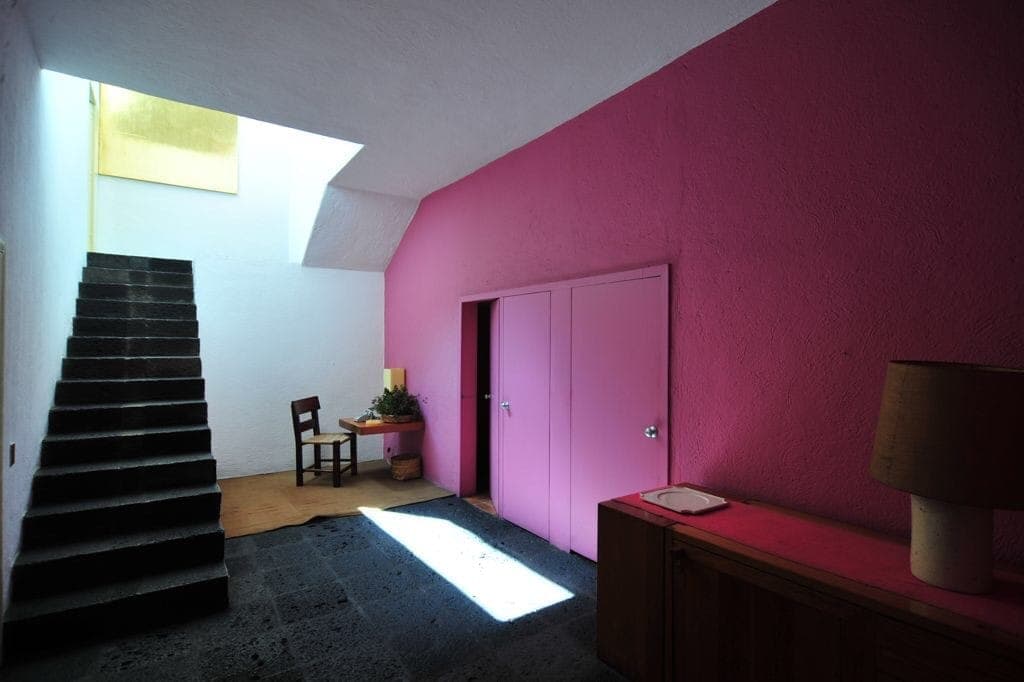 ภายใน Casa Luis Barragán ที่มีผนังสีชมพูโดดเด่น เฟอร์นิเจอร์มินิมอล บันไดสีเข้ม และแสงธรรมชาติส่องลงมาจากด้านบน