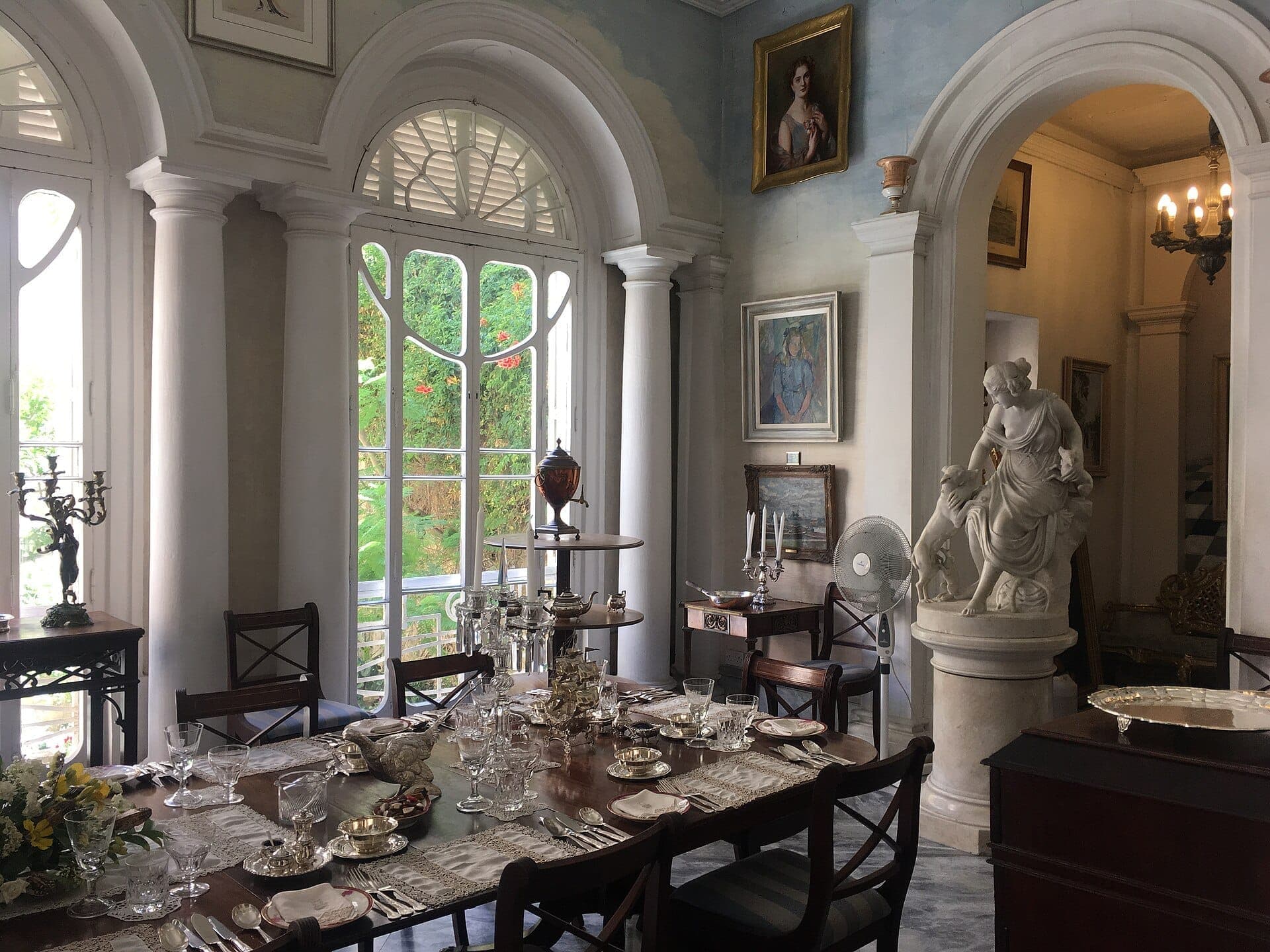 Elegantes Esszimmer in Casa Rocca Piccola mit einem gedeckten Tisch, klassischer Statue, Bogenfenstern und hereinströmenden Tageslicht.