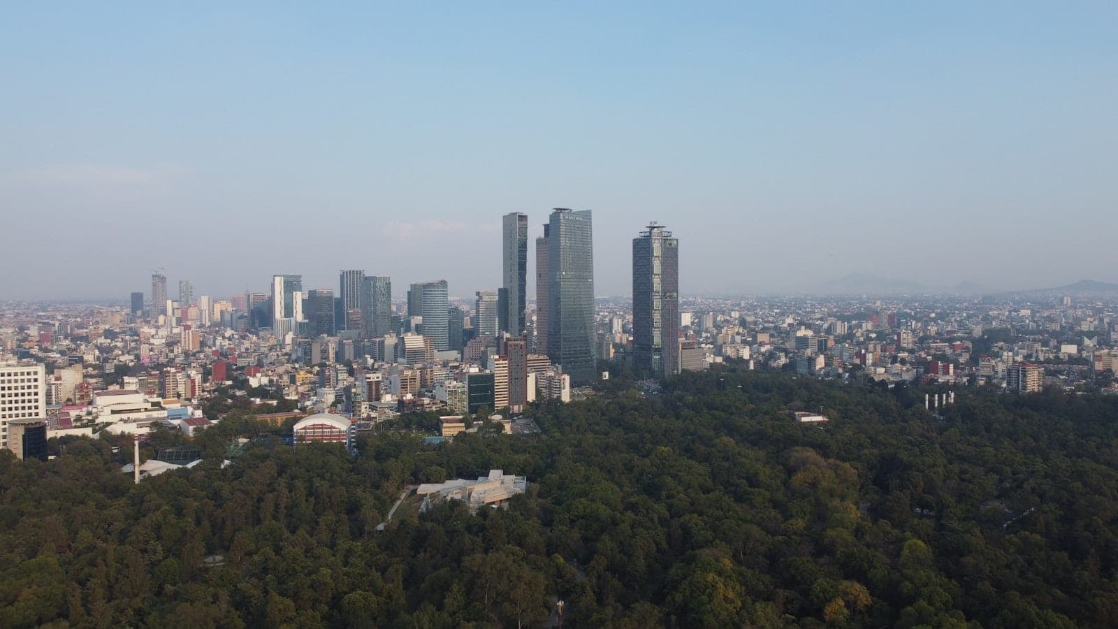 ภาพถ่ายมุมสูงเมืองเม็กซิโกซิตี้ เห็นผืนป่าสีเขียวของ Bosque de Chapultepec ด้านหน้า และเส้นขอบฟ้าของโปลังโกยุคใหม่เบื้องหลังในวันที่อากาศปลอดโปร่ง
