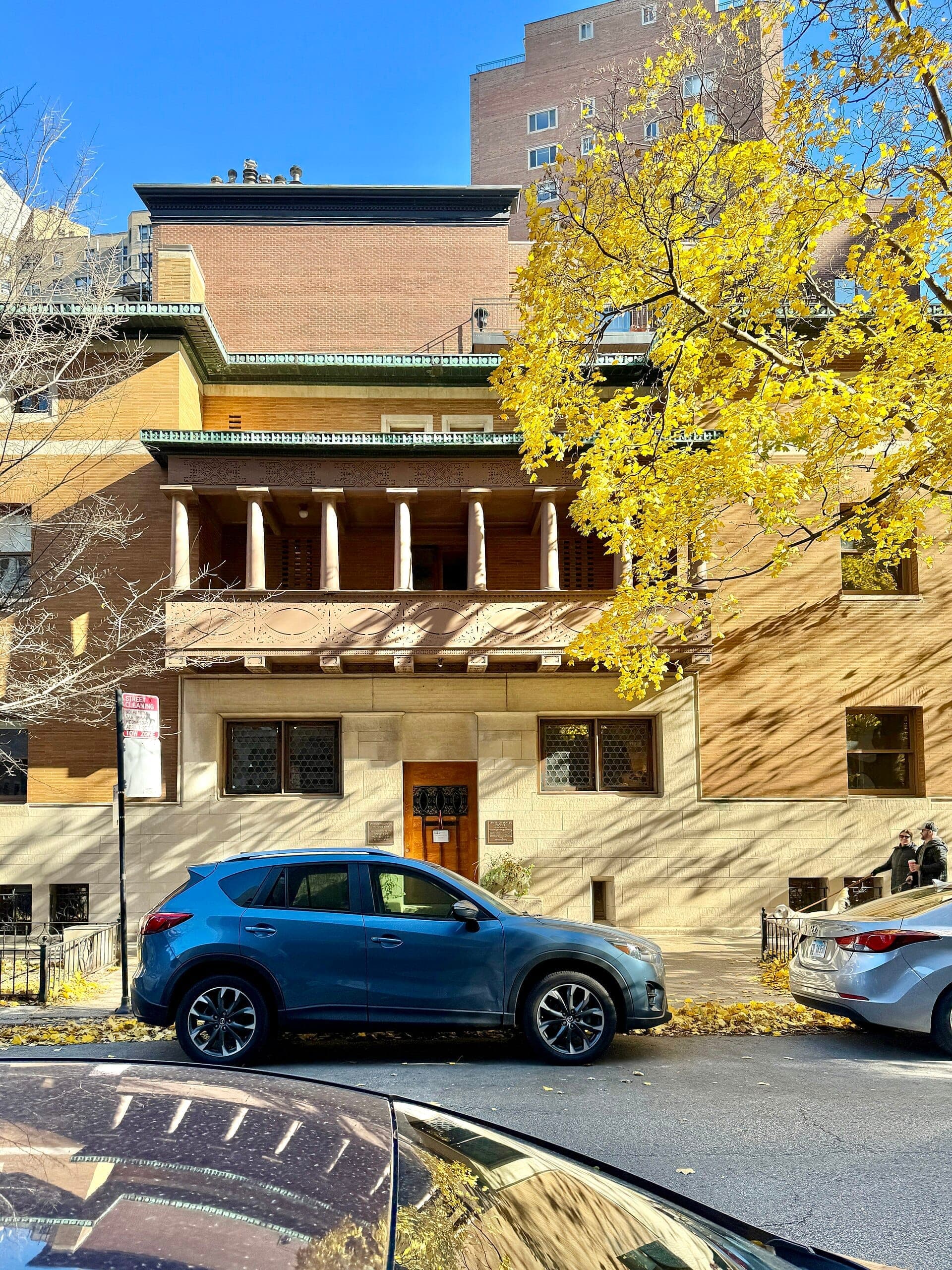 Front view of the Charnley-Persky House Museum with autumn trees, classic brick and stone facade, and parked cars along the street.