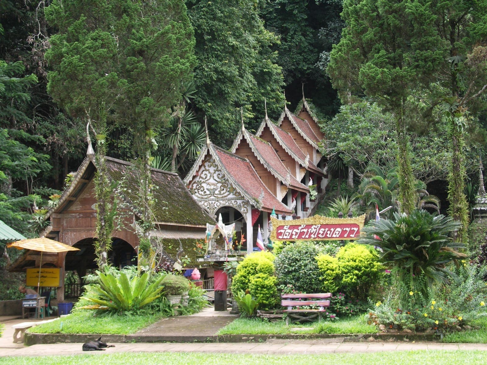 Traditionelle thailändische Tempelgebäude mit roten Ziegeldächern und kunstvollen Schnitzereien am Eingang zur Chiang Dao Cave, umgeben von üppigem Grün.