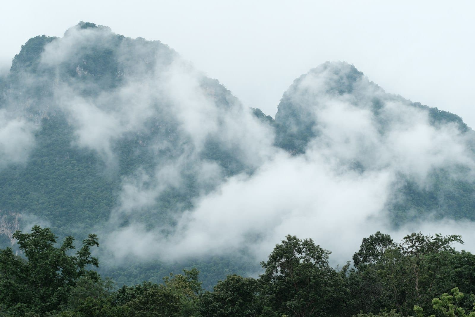 Nebelverhangene Kalksteinberge mit üppig grünen Bäumen im Vordergrund – die stille, naturbelassene Schönheit von Chiang Dao.