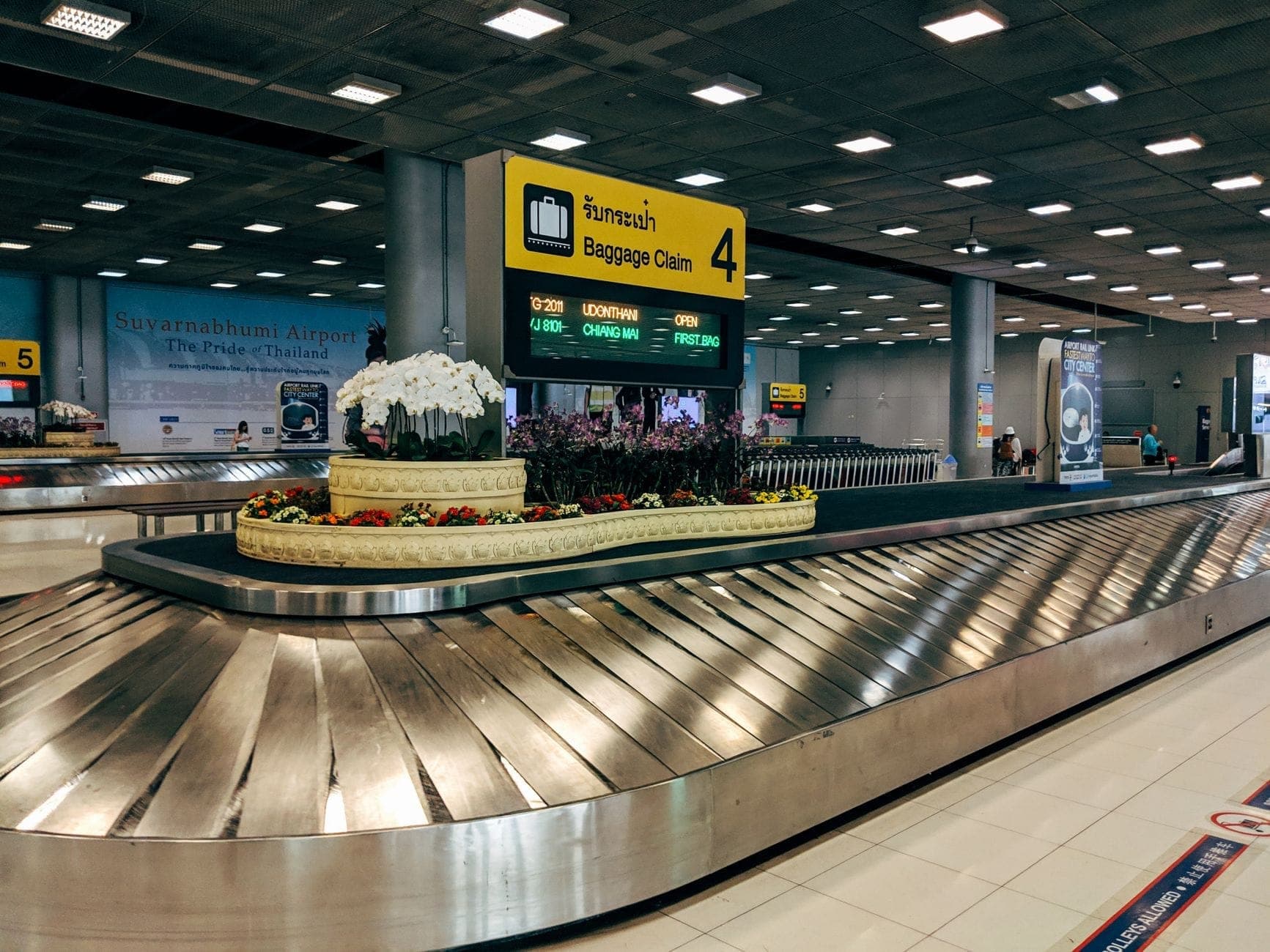 Área de recogida de equipaje en el interior del Aeropuerto de Chiang Mai con un cartel visible en tailandés e inglés, dando la bienvenida a los pasajeros que llegan a la terminal.