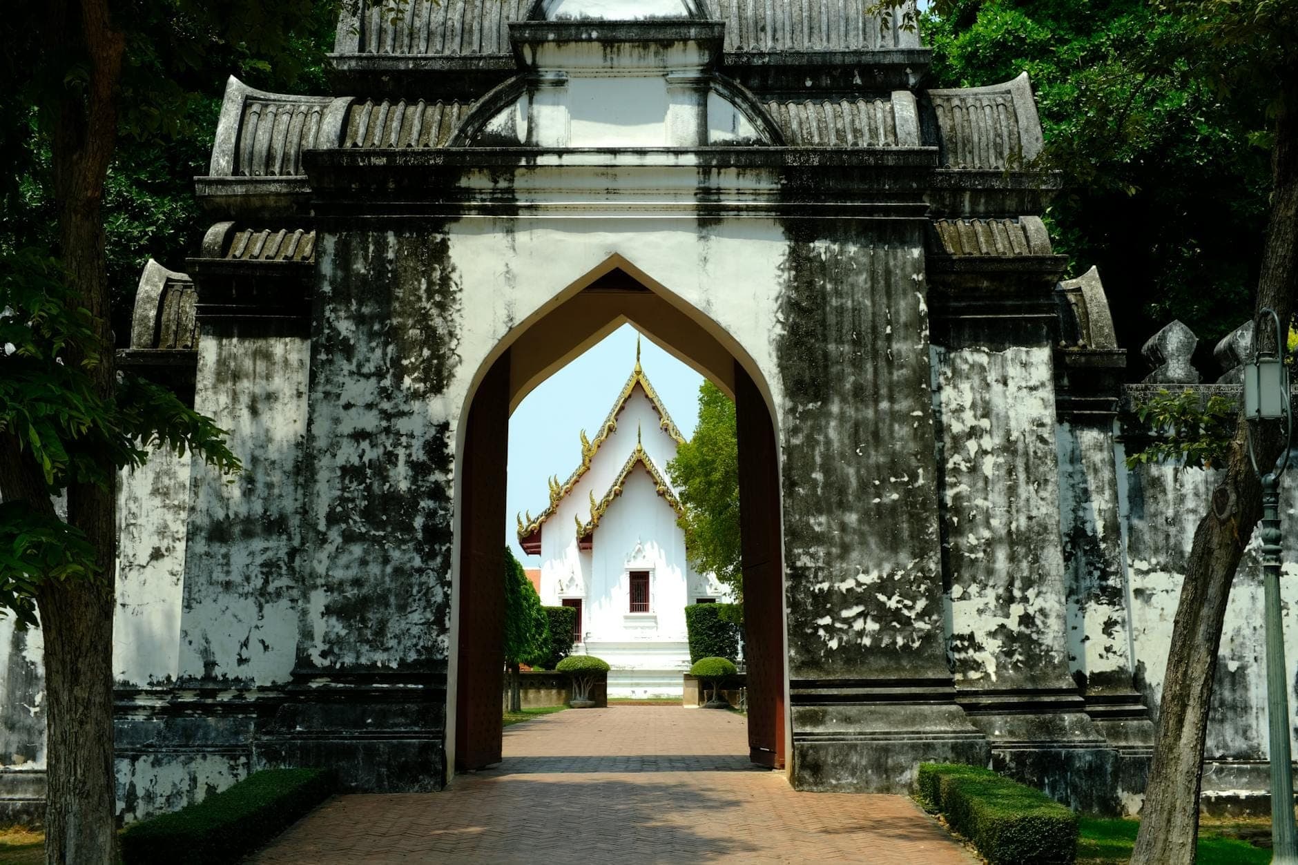 Storico portale bianco con ingresso ad arco e vista su un edificio del patrimonio sullo sfondo, circondato da verde a Chiang Mai.