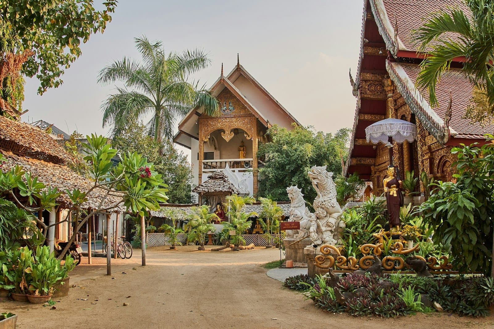 Widok Starego Miasta Chiang Mai z historycznymi świątyniami z drewna tekowego i ogrodową atmosferą, z tropikalnymi roślinami i tradycyjnymi posągami.
