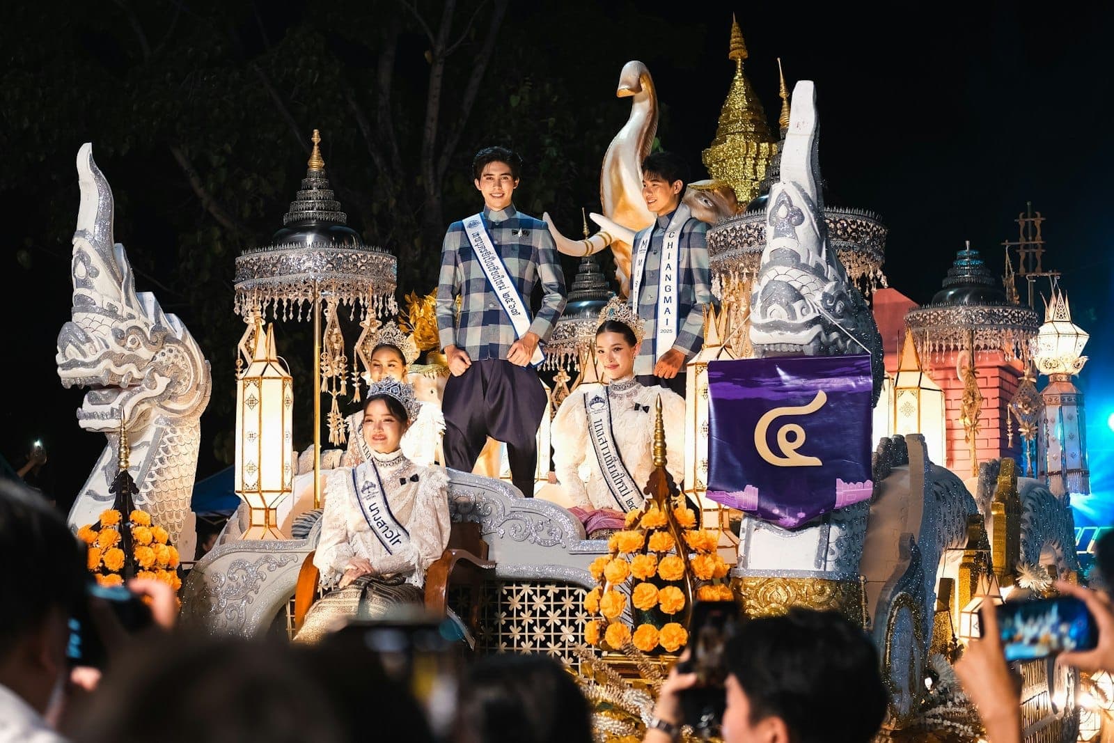 Aufwendig geschmückter Festumzugswagen beim Chiang Mai Blumenfestival mit Menschen in traditionellen Gewändern und leuchtenden Blumendekorationen bei Nacht.