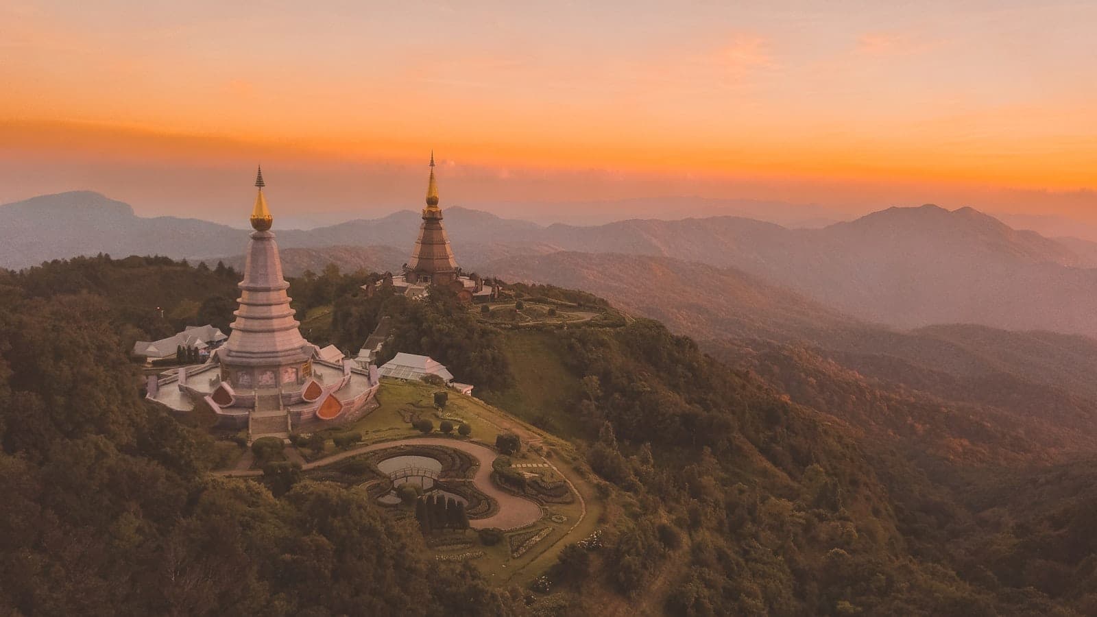 Widok z lotu ptaka na dwie zdobne pagody na bujnym górskim grzbiecie o zachodzie słońca w Chiang Mai, otoczone mglistymi wzgórzami i dramatycznym złotym niebem.