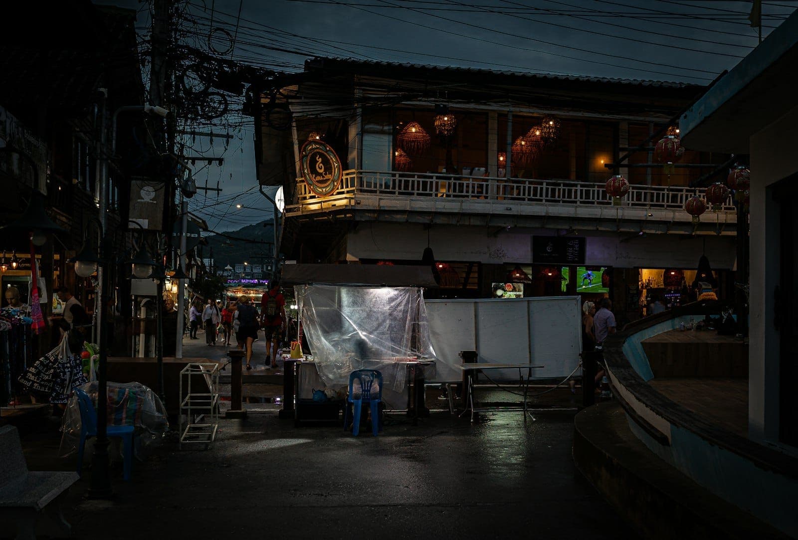 Scena uliczna w Chiang Mai o zmierzchu z ożywionym budynkiem ozdobiony lampionami, pieszymi i gwarną, a zarazem kameralną atmosferą wieczoru.