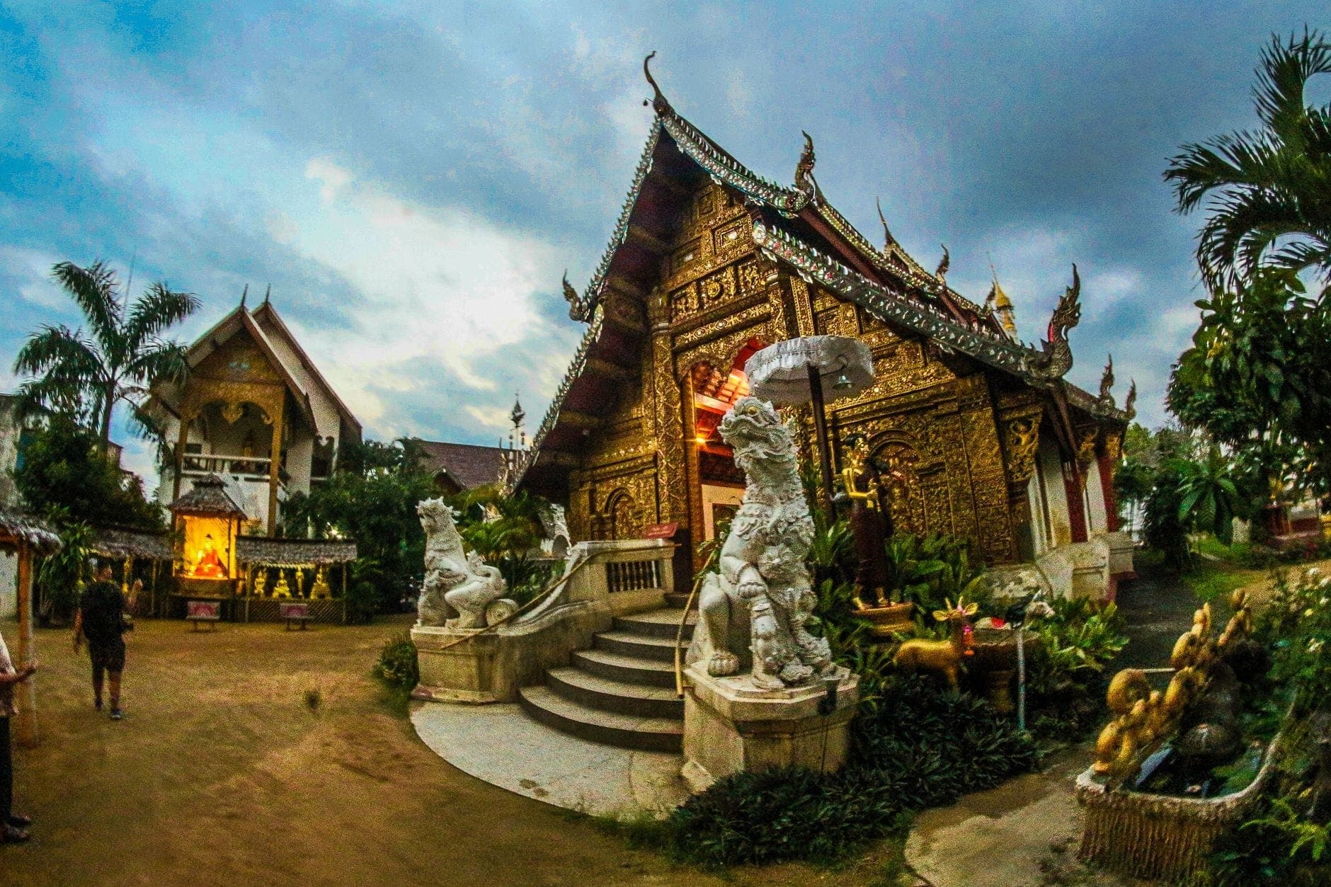 Kleiner, reich verzierter Tempel in Chiang Mai mit goldenen Details und Wächterfiguren, umgeben von üppigem Grün in einer ruhigen, stimmungsvollen Umgebung.