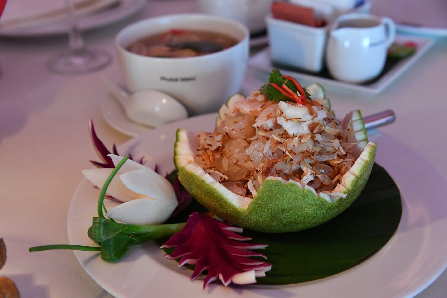 Elegante piatto tailandese con cibo finemente preparato servito in un pomelo intagliato, con guarnizioni artistiche di verdure, su un tavolo di ristorante.